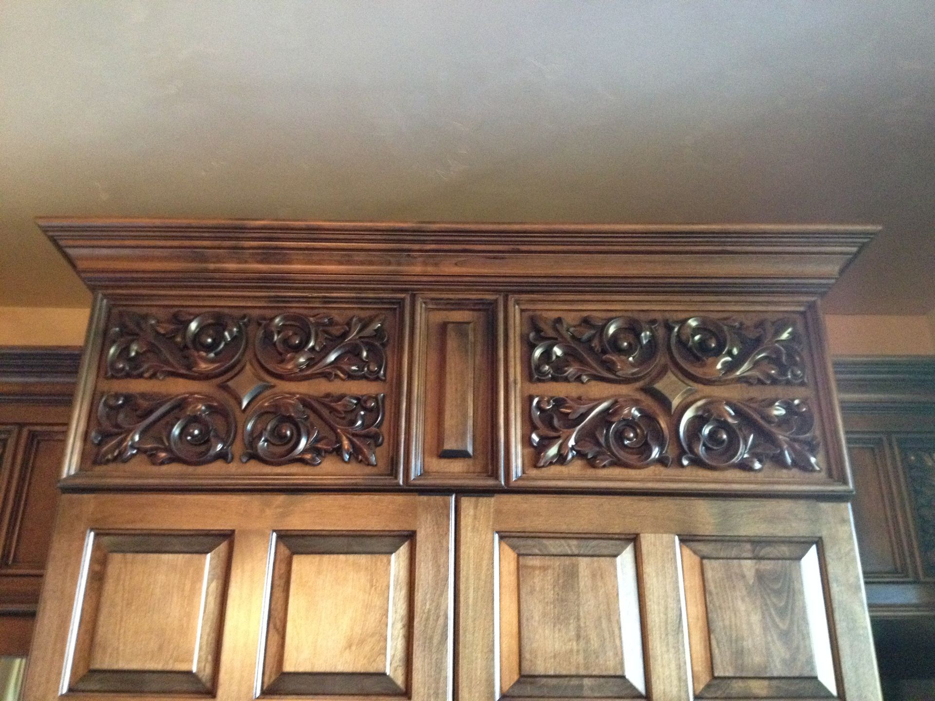 Wooden kitchen cabinets with intricate carved panels and decorative crown molding.