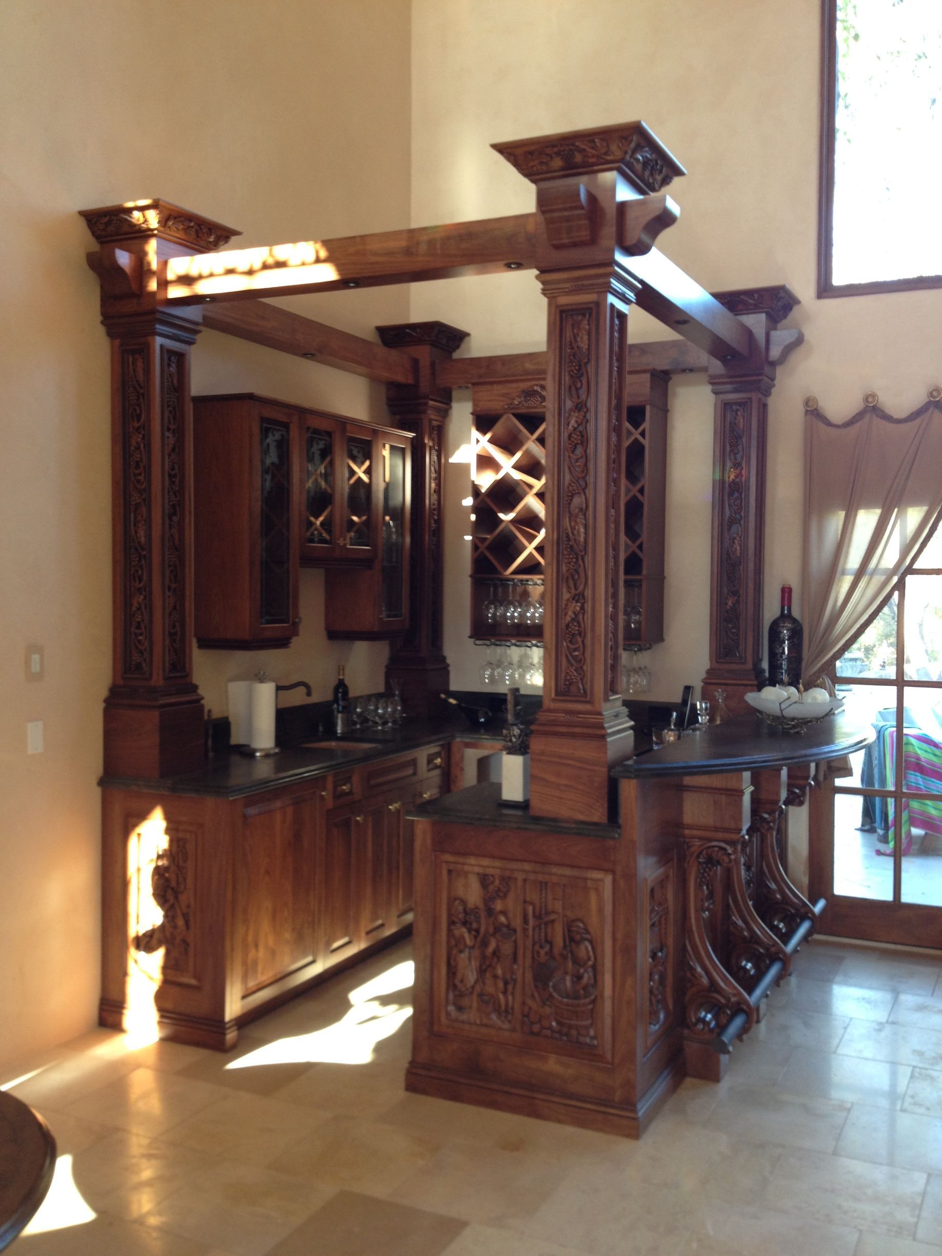 Ornate wooden bar with built-in cabinetry, wine rack, and countertops, under a beam structure.