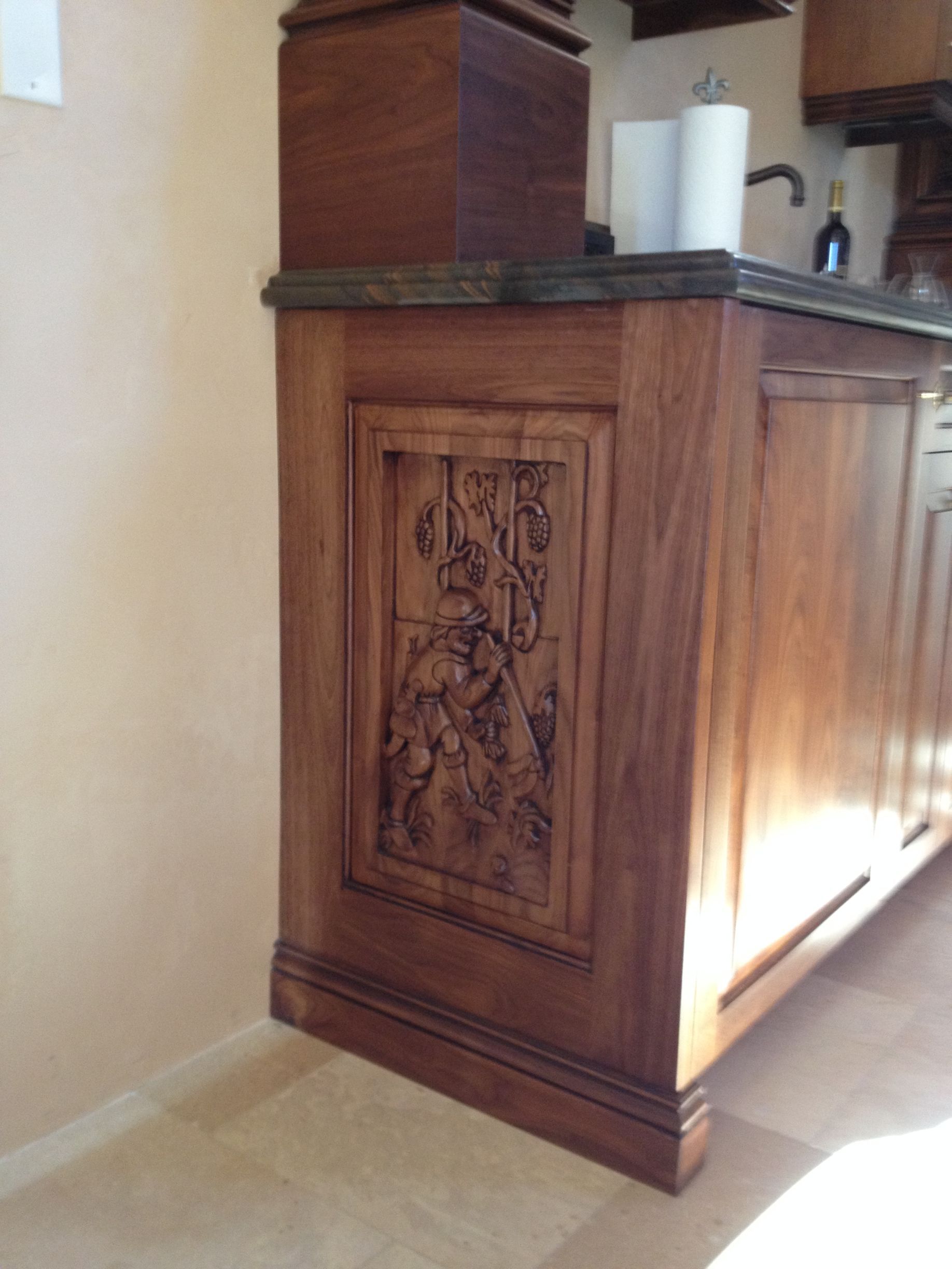 Wooden kitchen island with carved panel; light wood cabinets and countertop, paper towels on top.