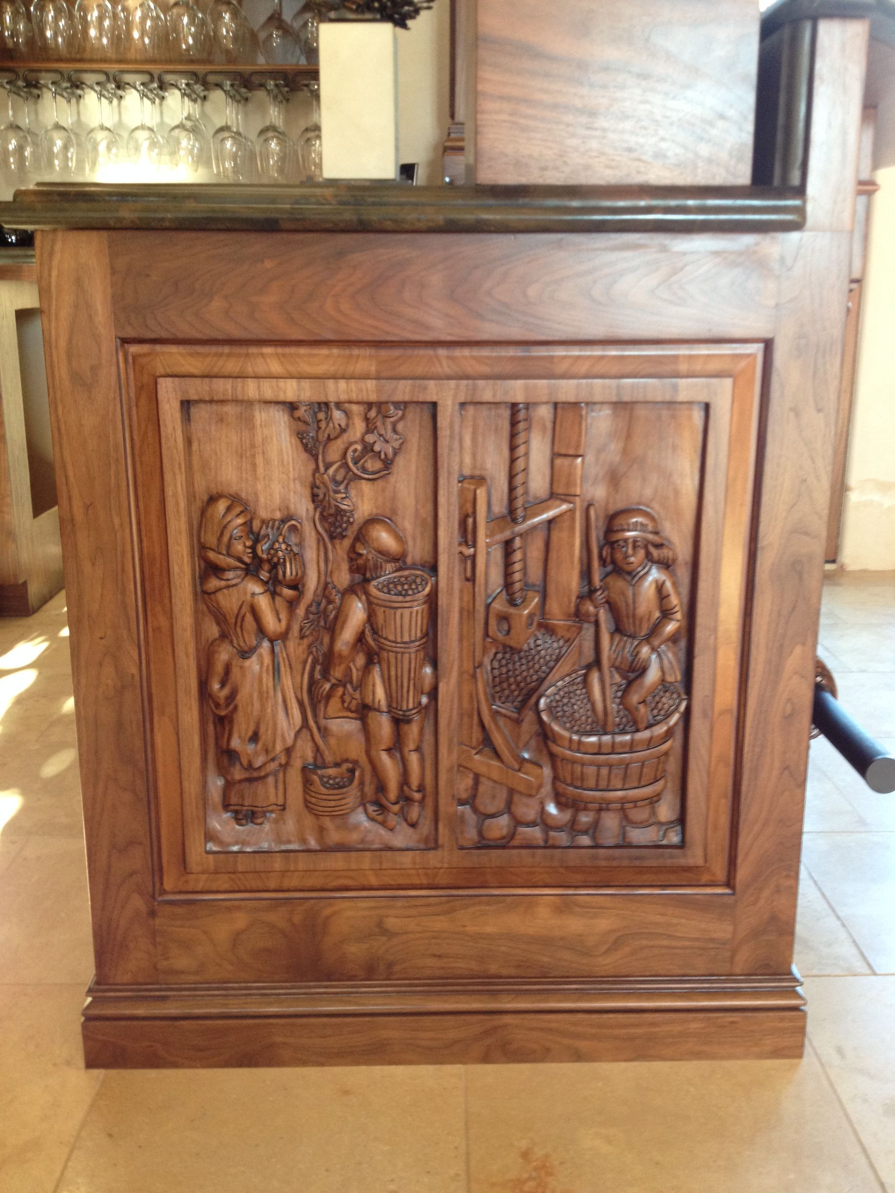 Wooden bar front with carved relief of figures harvesting grapes and pressing juice.