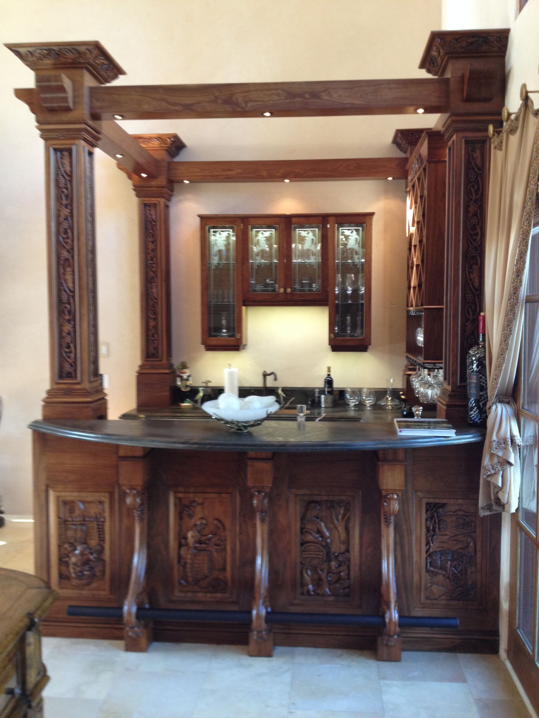 Wooden bar with carved details, built-in cabinets, and a dark countertop.