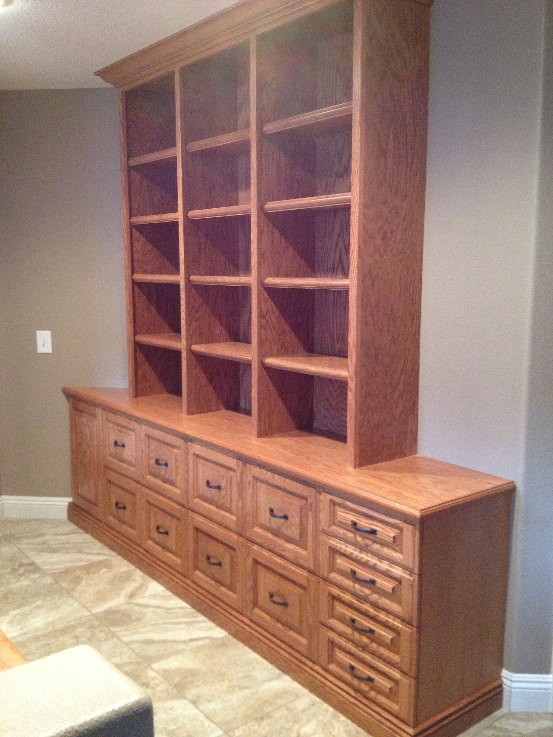 Wooden built-in shelving unit with drawers below. Brown wood against a tan wall, on tile floor.