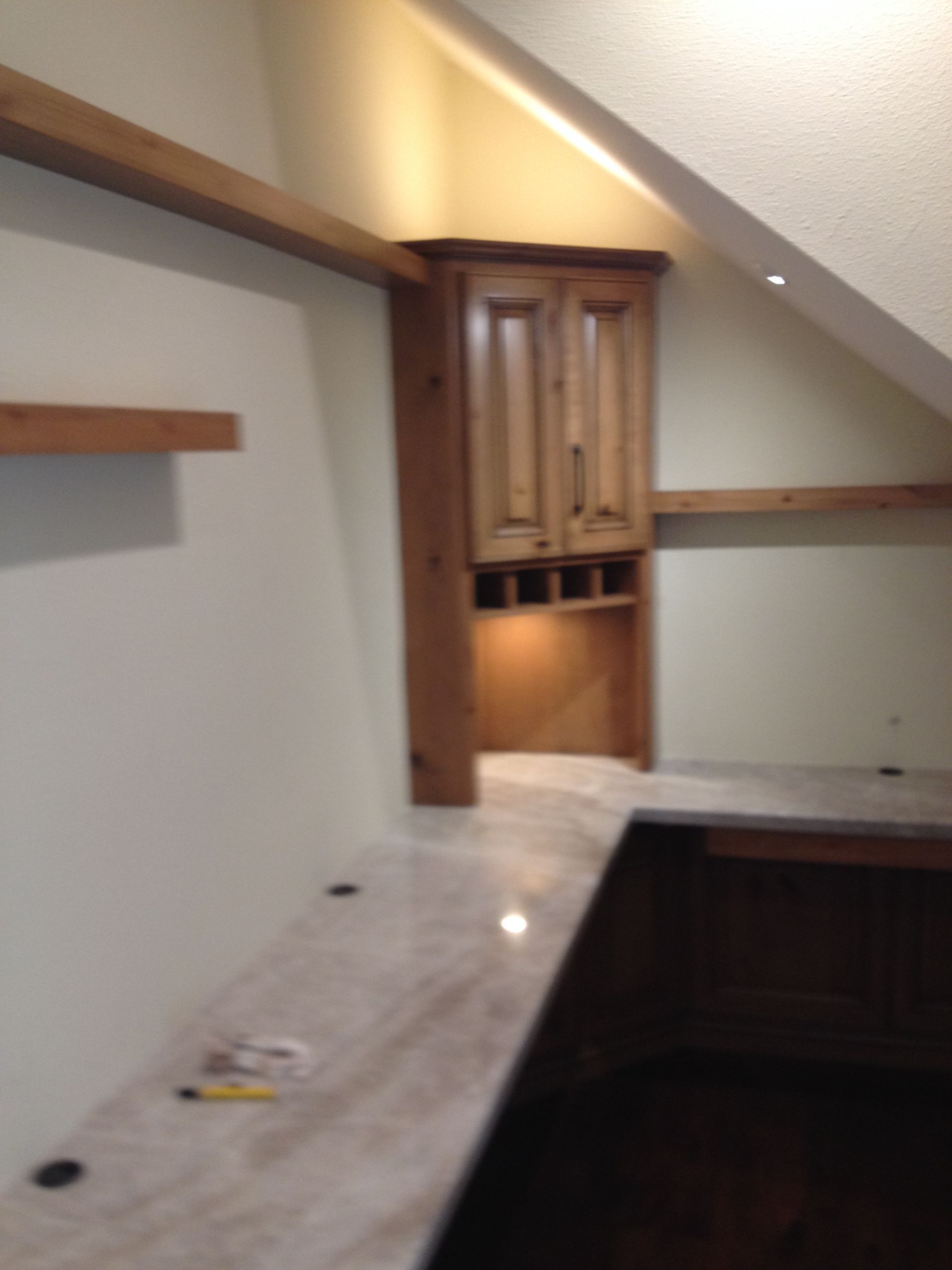 Built-in wooden cabinet with wine rack in a corner, above a countertop with lights.