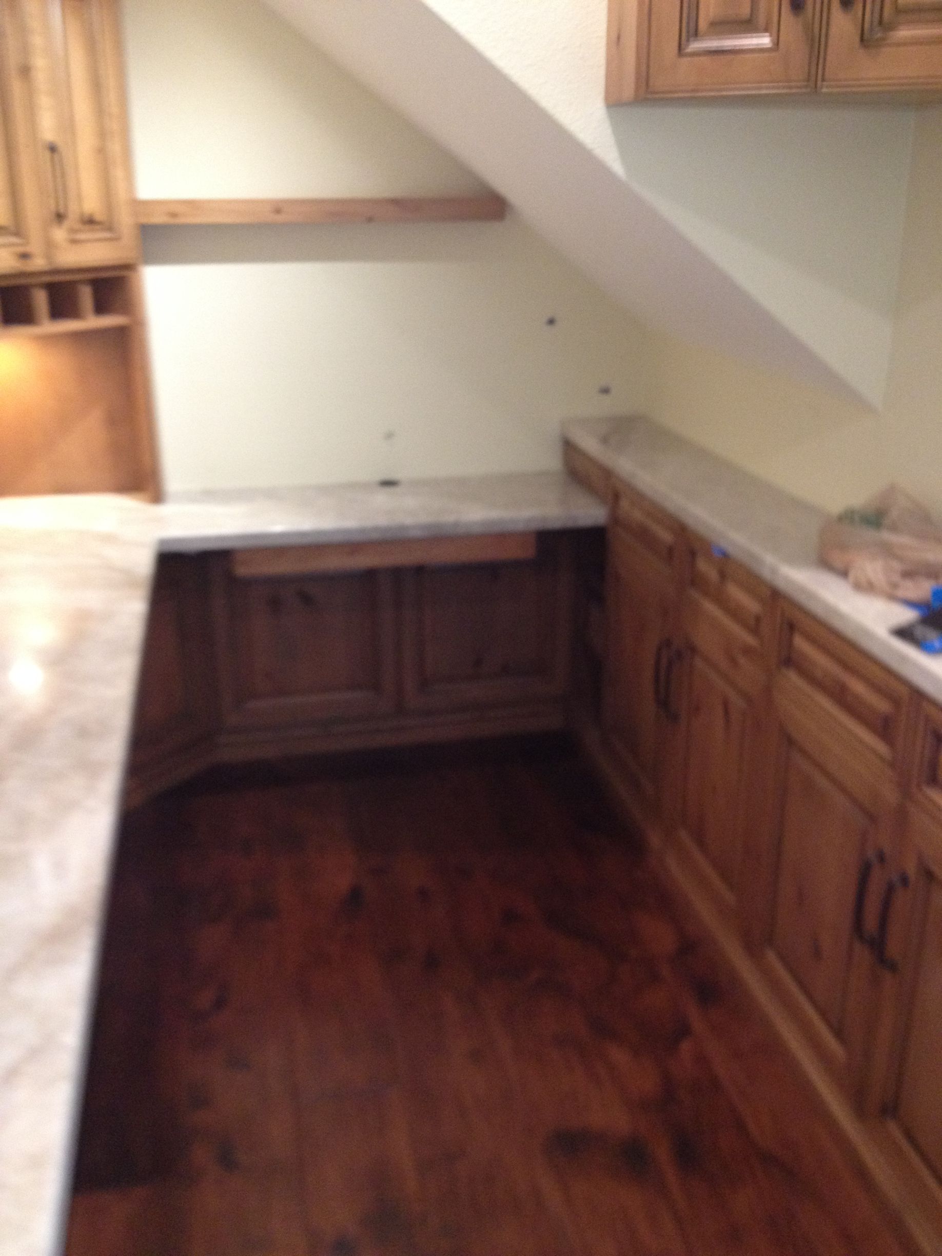 A kitchen with wooden cabinets, countertops, and flooring. An angled wall is above the counter.