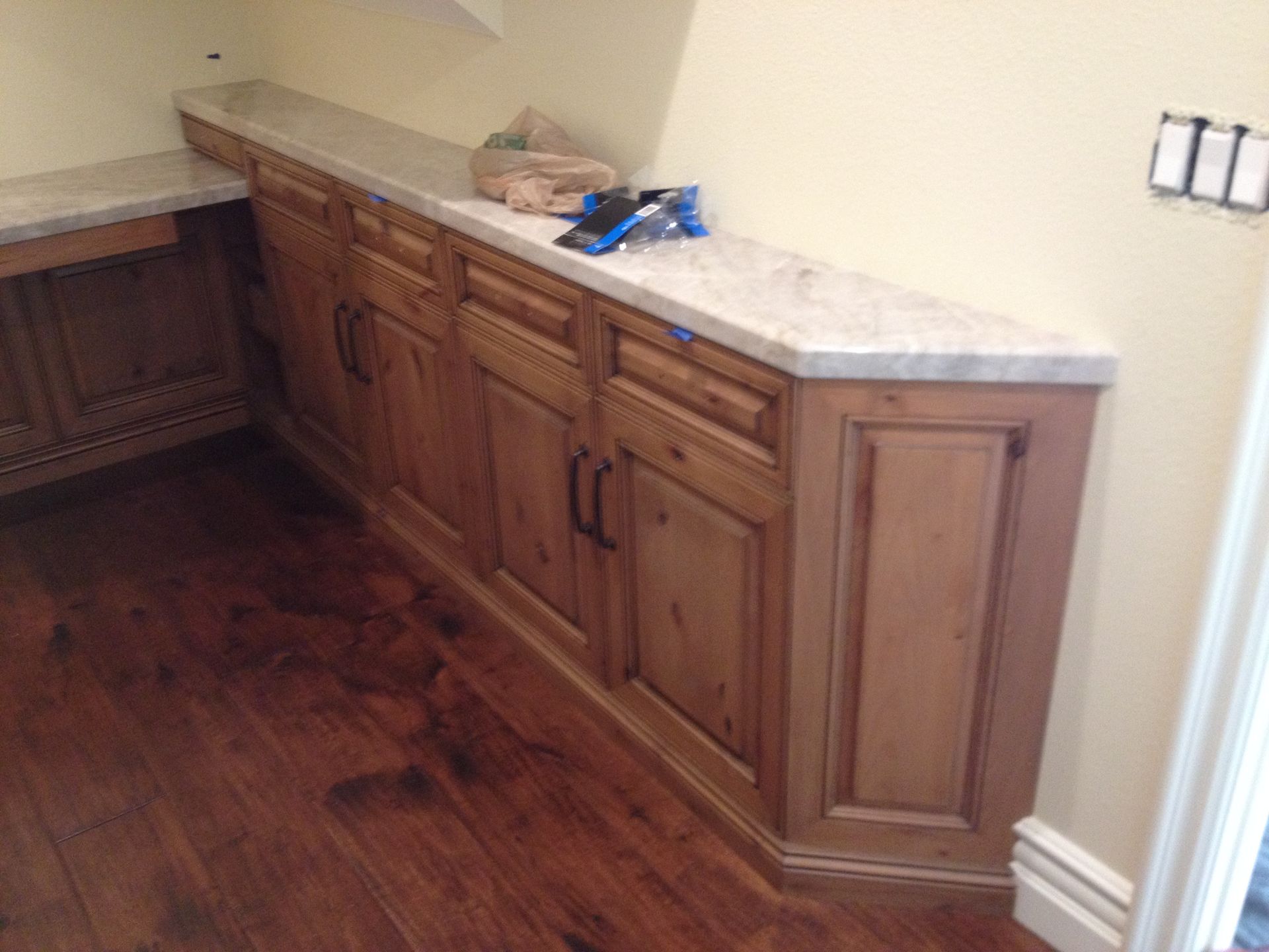 Wooden cabinets with a light countertop in a corner, installed near a wood floor and beige wall.