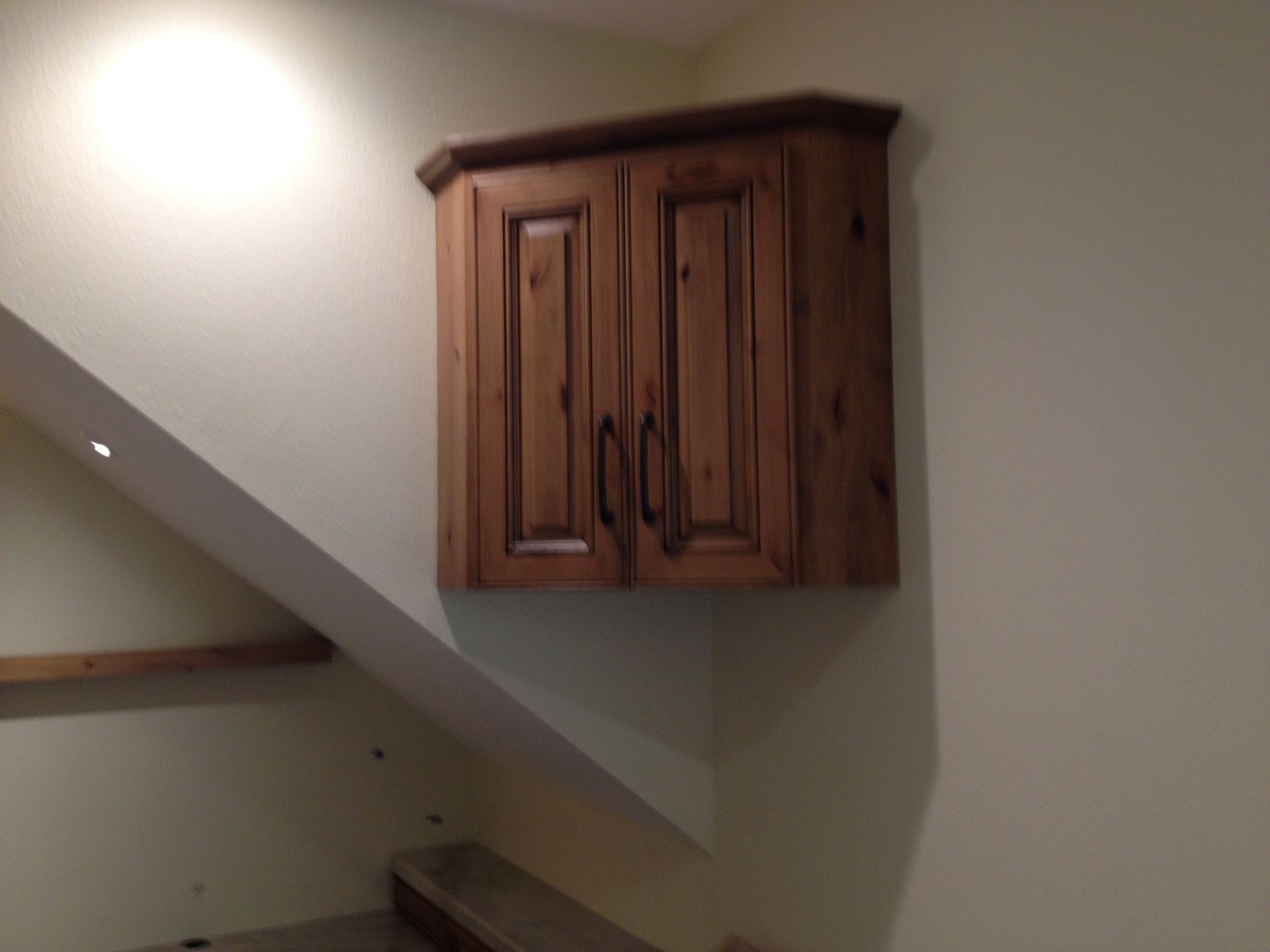 Wooden corner cabinet mounted on a cream-colored wall, above a slanted wall and ledge.