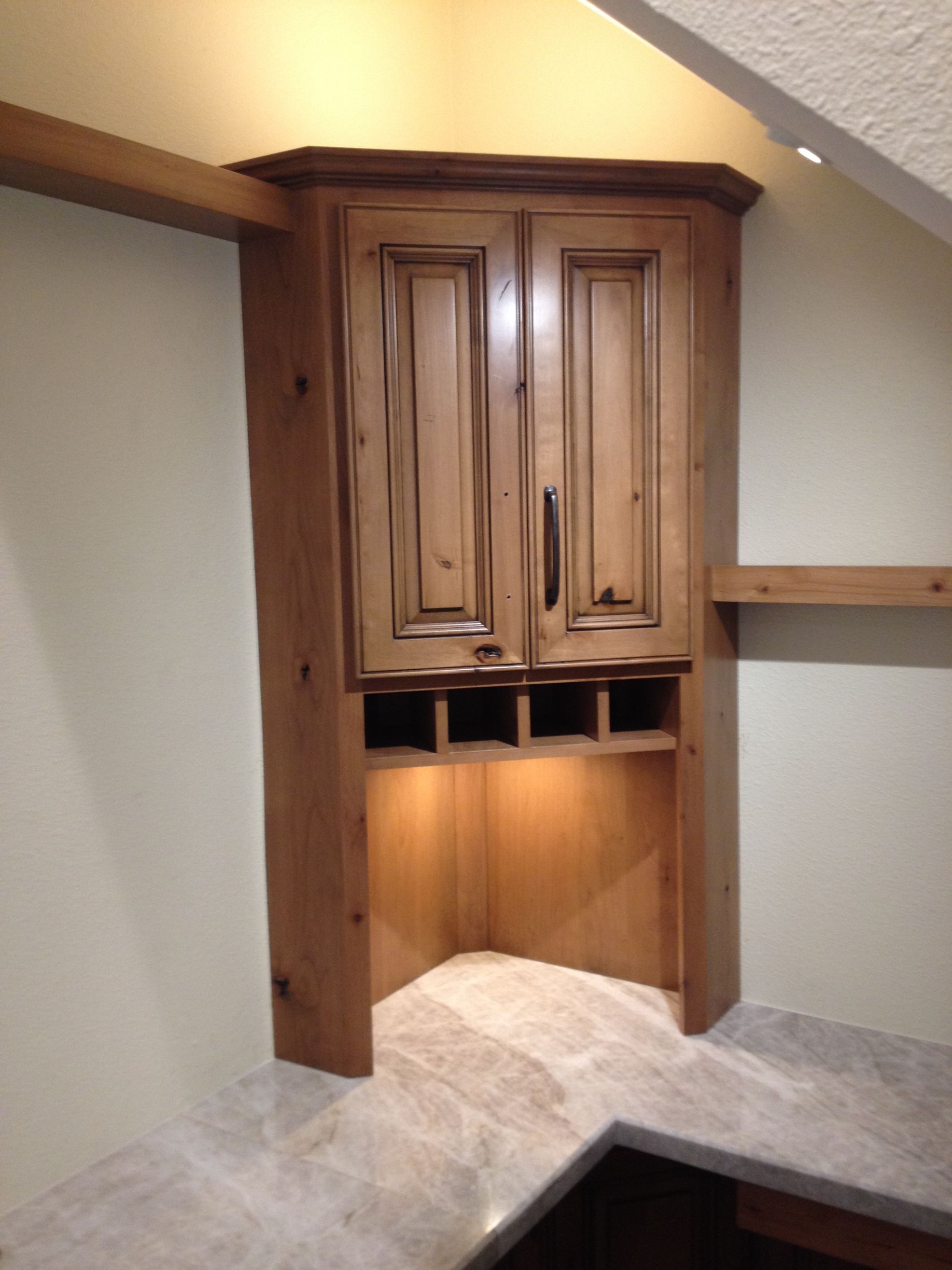 Corner cabinet with wine rack, lit from within, set into beige walls, above a light-colored countertop.