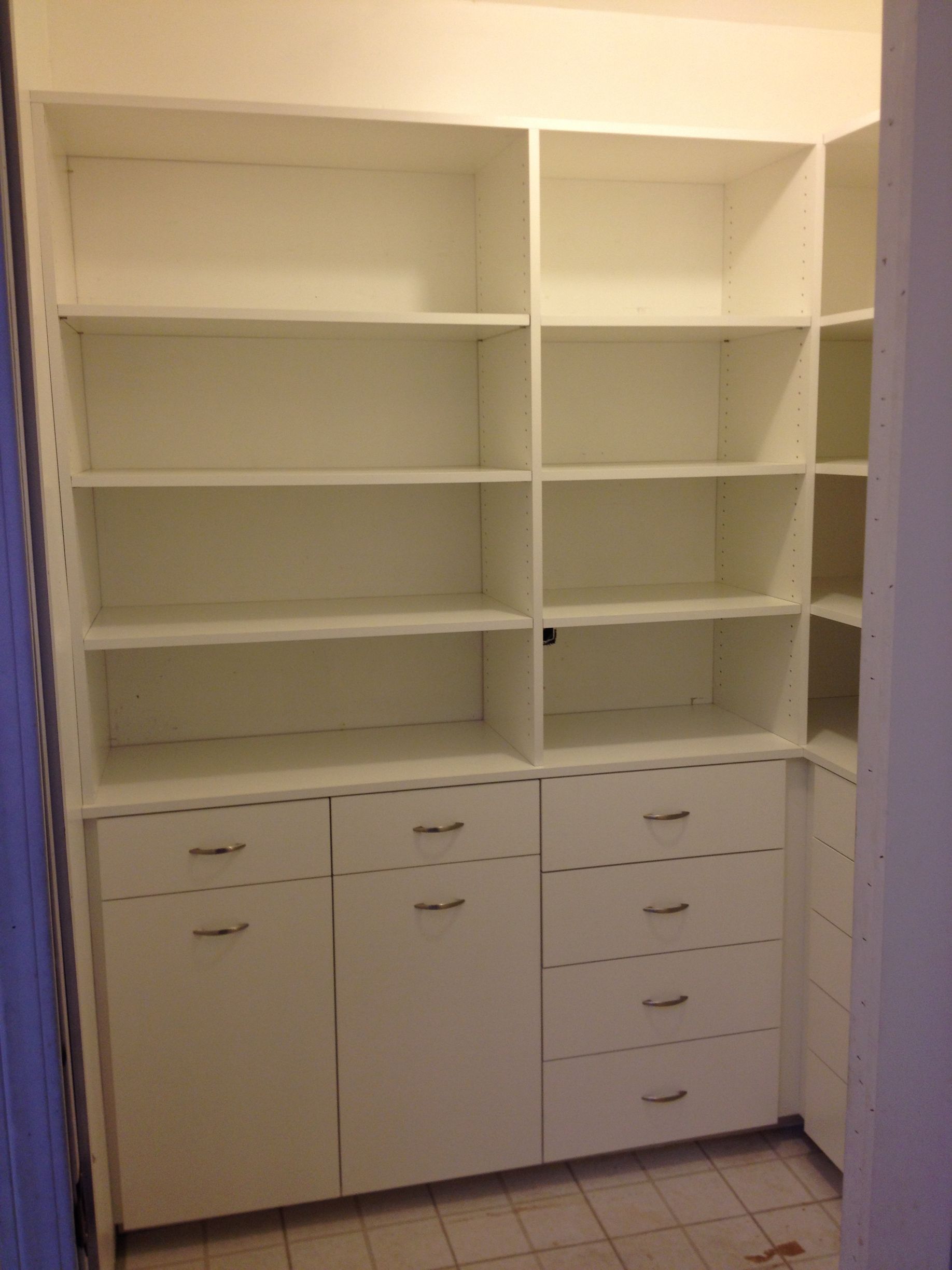 White built-in closet with shelves, drawers, and cabinet doors in a corner.