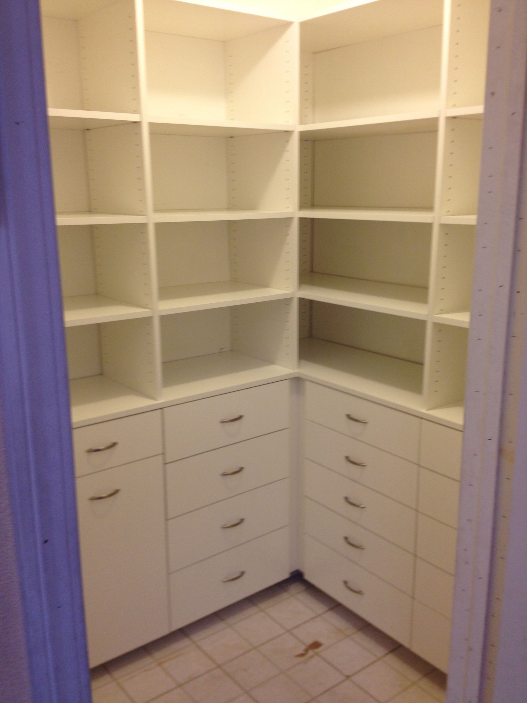 Empty white closet with built-in shelves and drawers in a corner.
