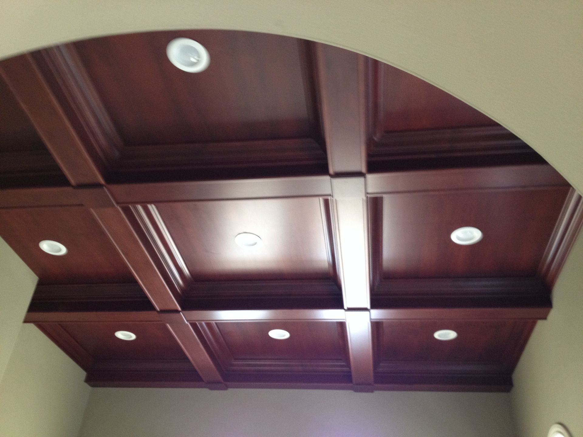 Coffered wood ceiling with recessed lights, archway, and beige walls.