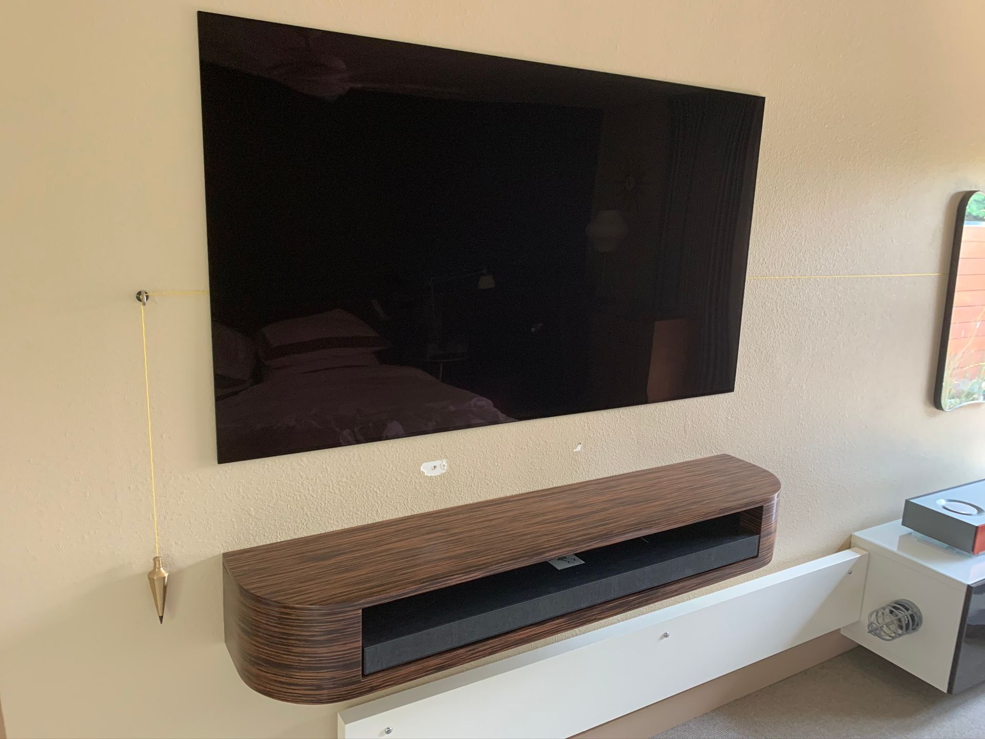 A wall-mounted TV above a floating wooden media console holding a soundbar. Beige wall.