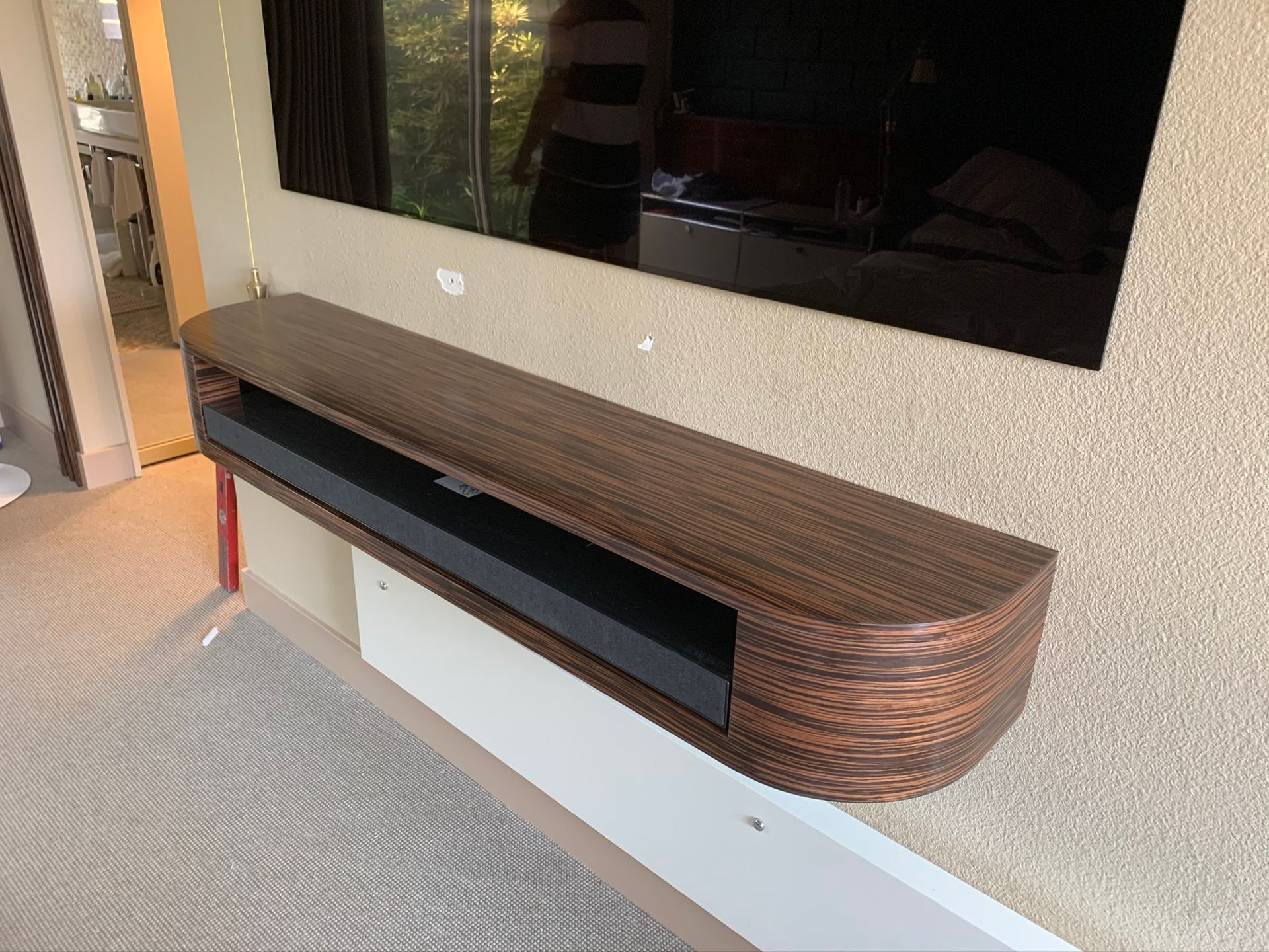 Wooden, wall-mounted entertainment console below a mounted TV on a textured wall.