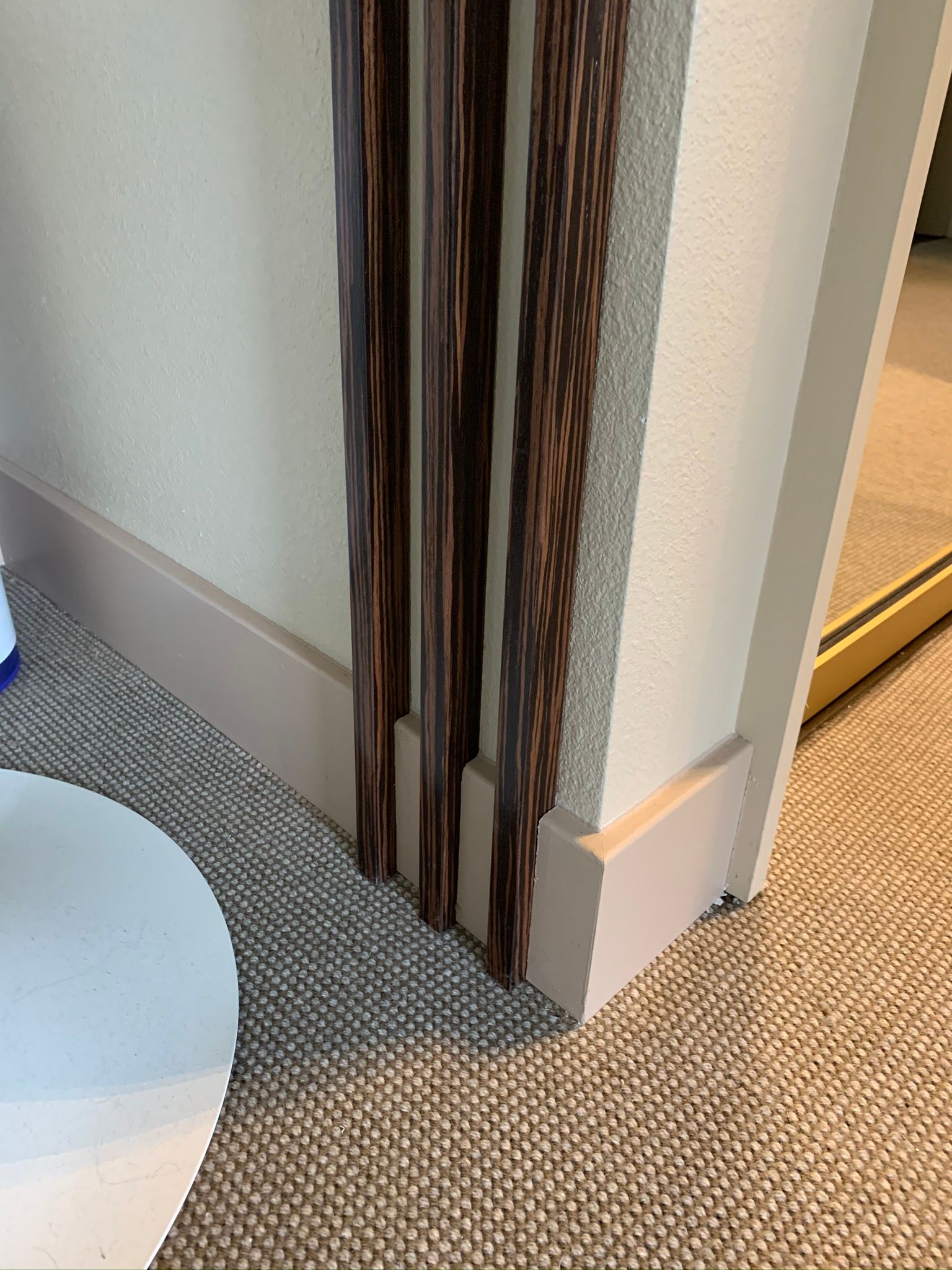 Wooden decorative panels on a wall with beige baseboard and carpeted floor.