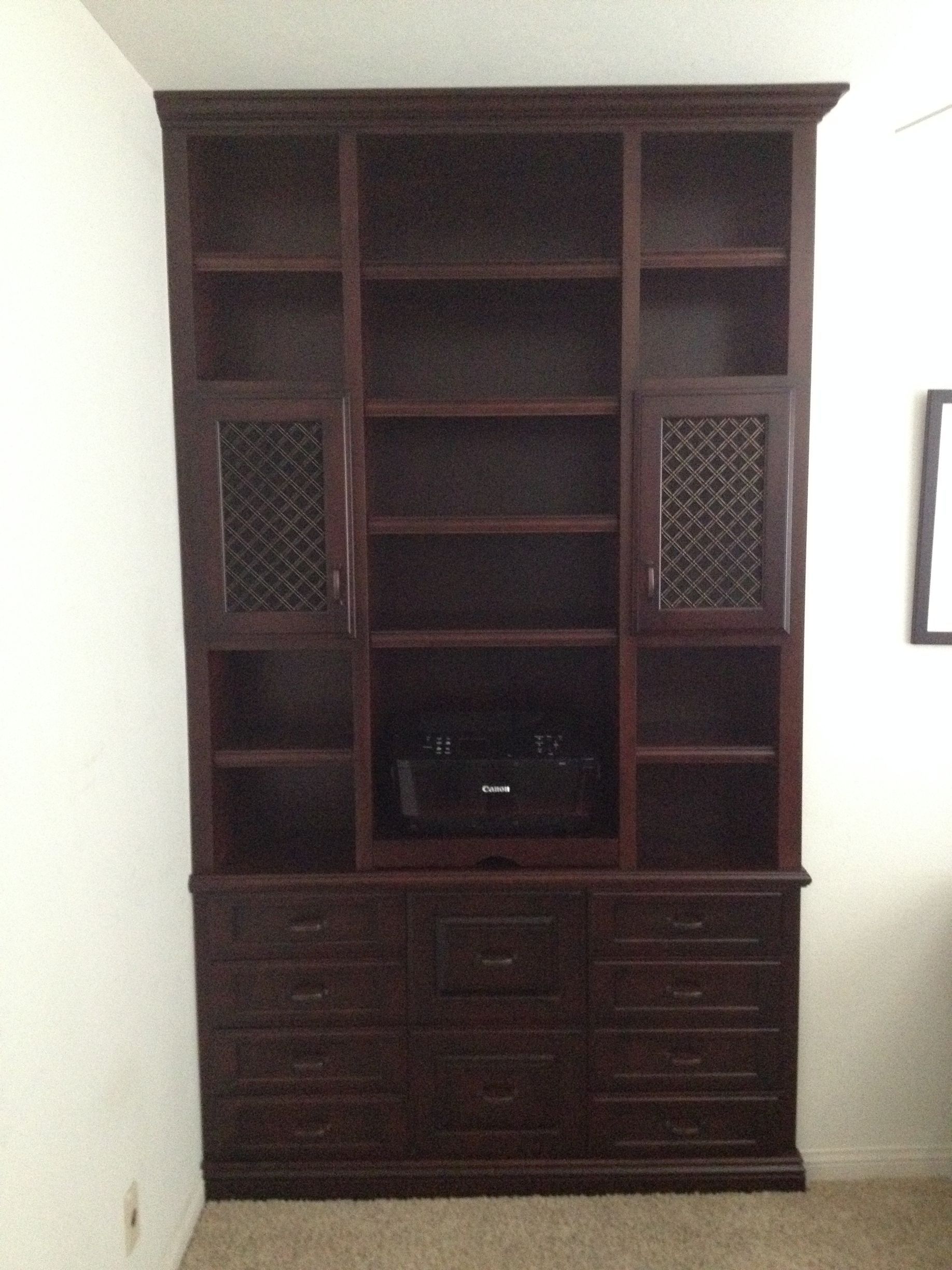 Dark wood built-in entertainment center with shelves, cabinets, and drawers against a light wall.