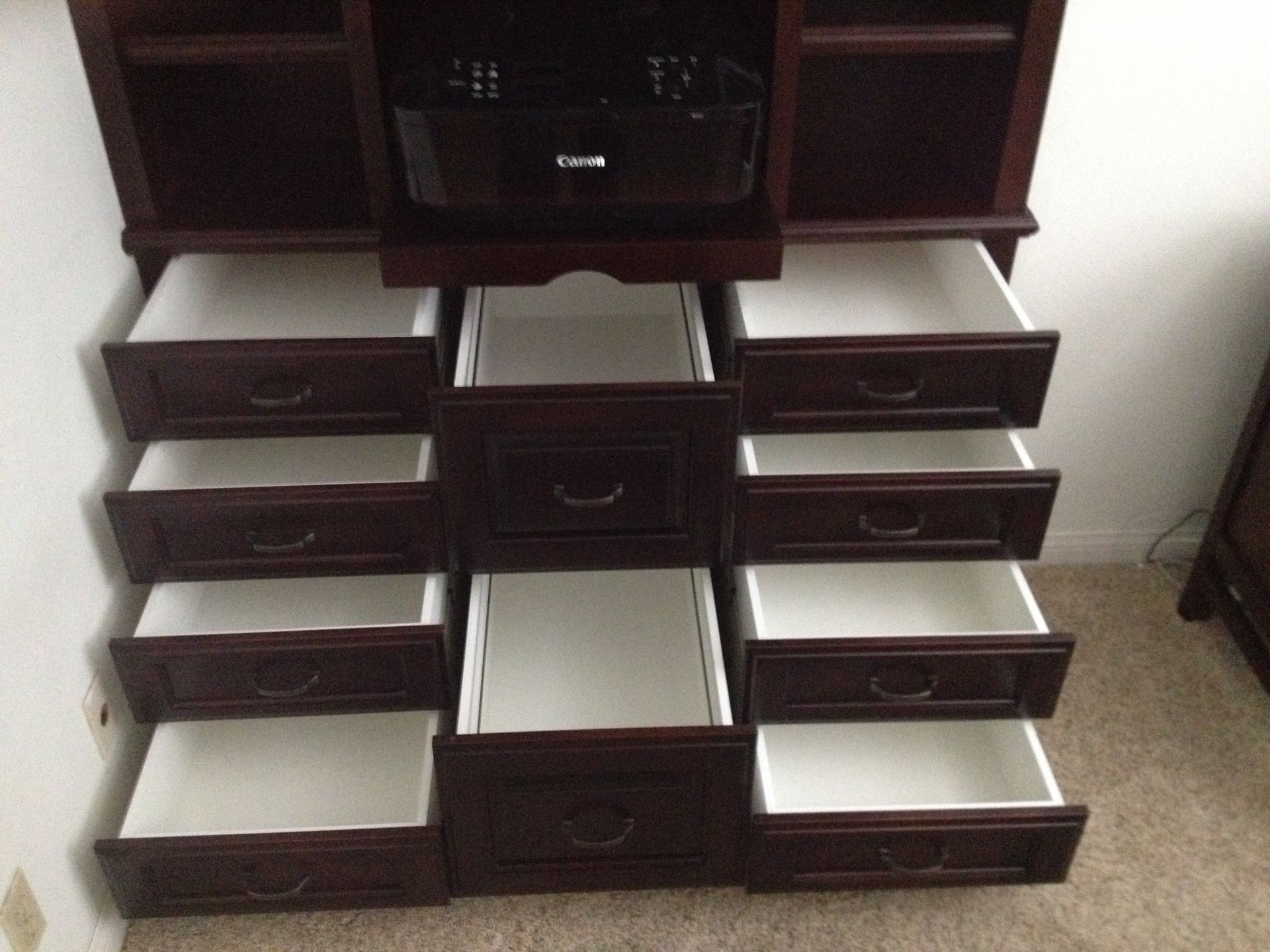Dark wood cabinet with multiple open drawers, white interiors.