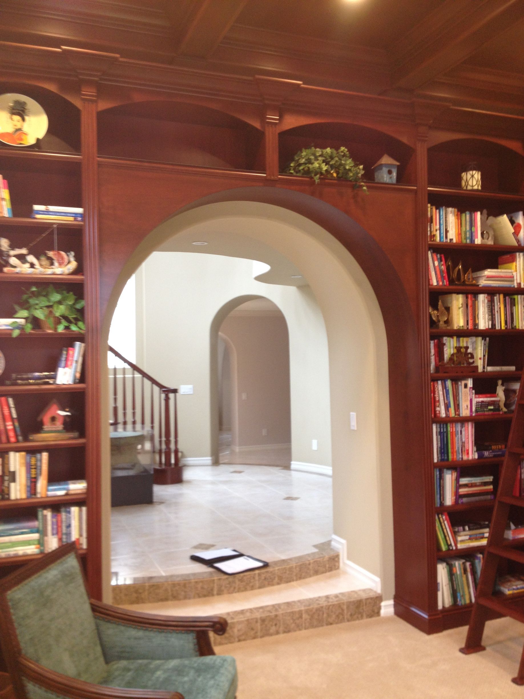 Library with arched doorway and built-in bookshelves. A green chair sits in the foreground.