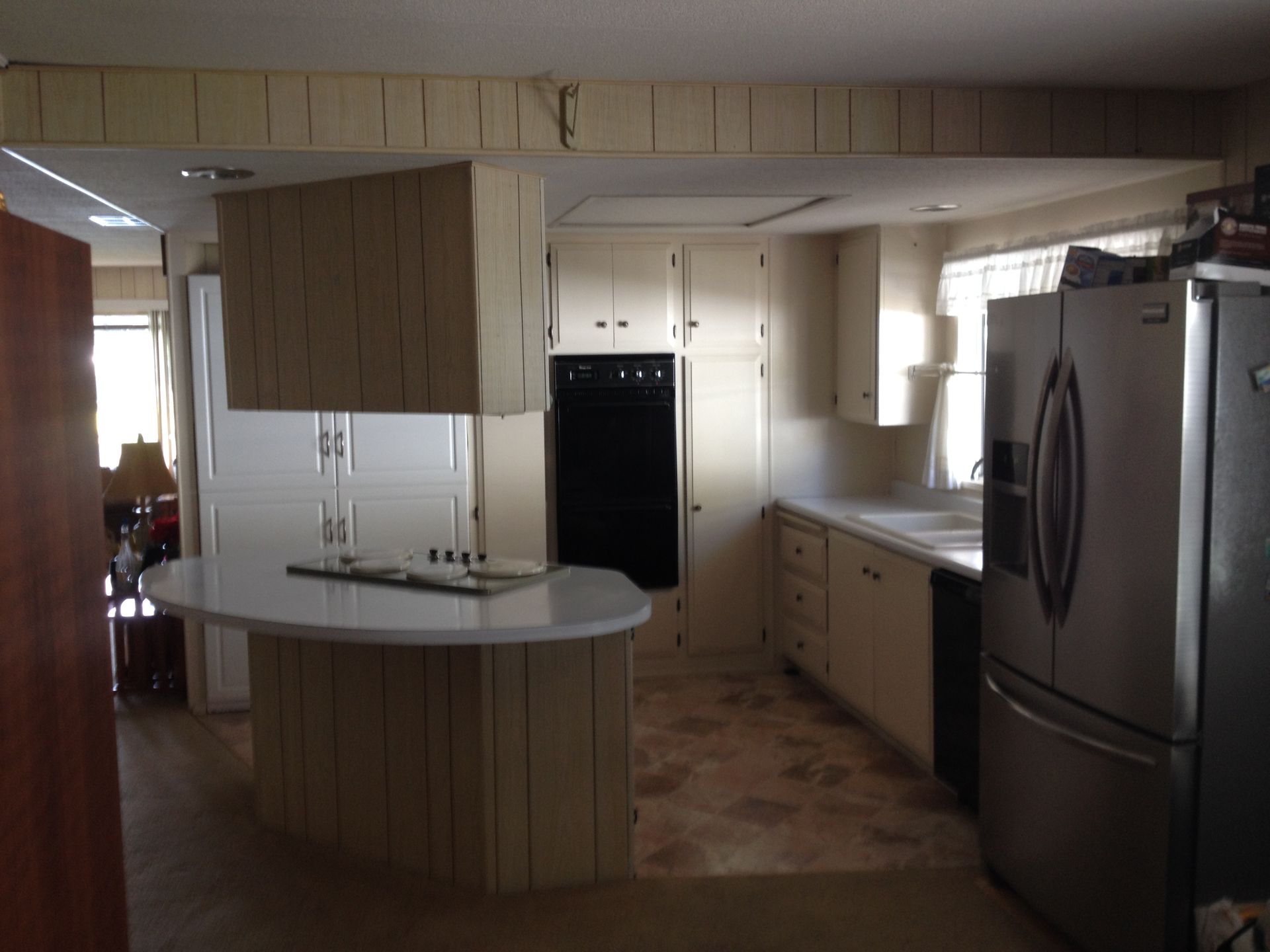 Kitchen with cream-colored cabinets, black oven, and stainless steel refrigerator. Oval island and patterned floor.