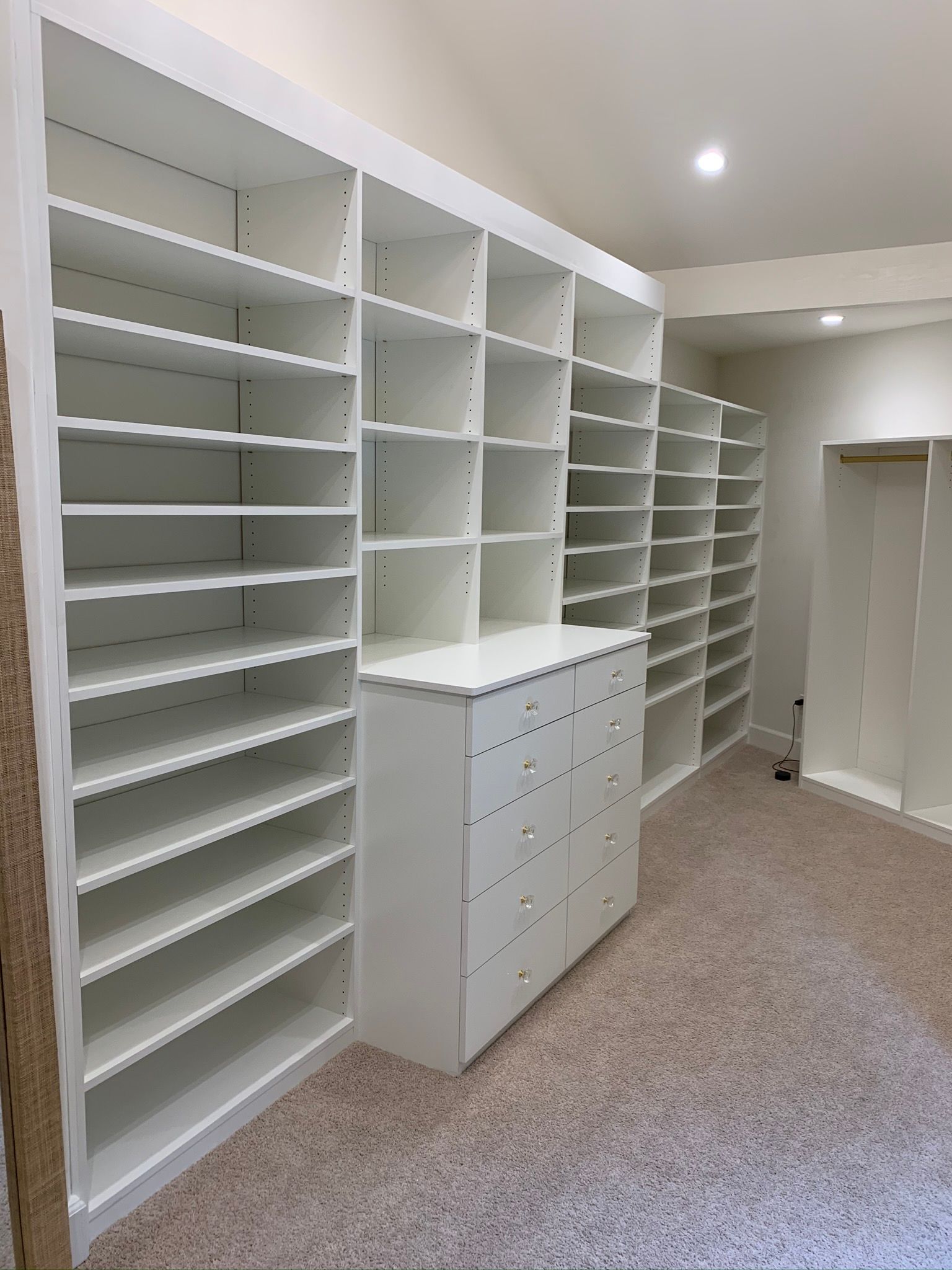 White built-in closet with shelves and drawers in a room with beige carpet.