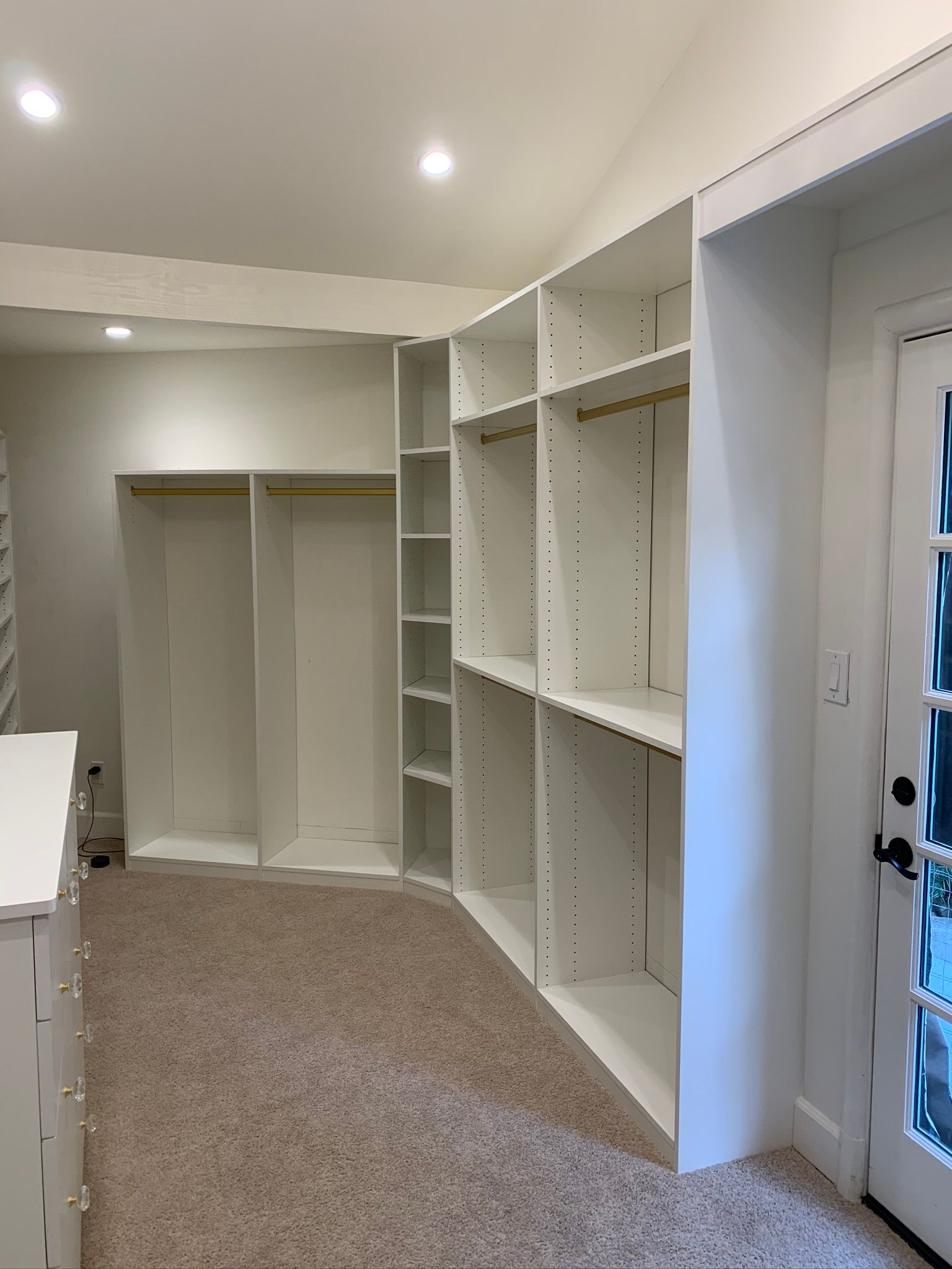 White closet organizers in a room with tan carpet and a door.