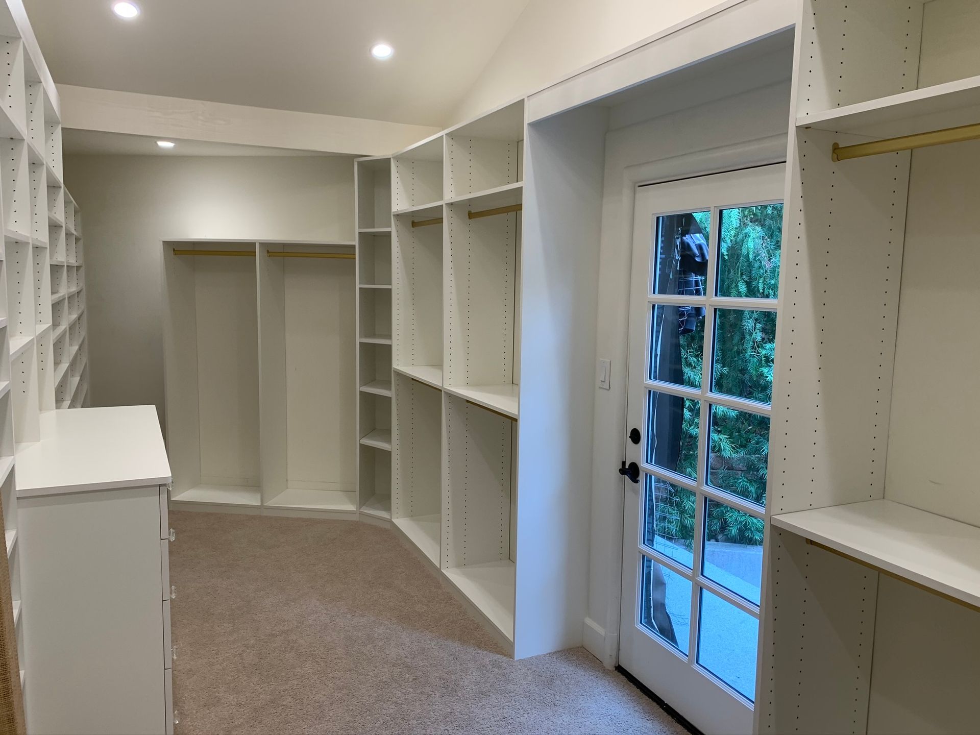 Walk-in closet with white shelves and door to outside with a view of greenery.