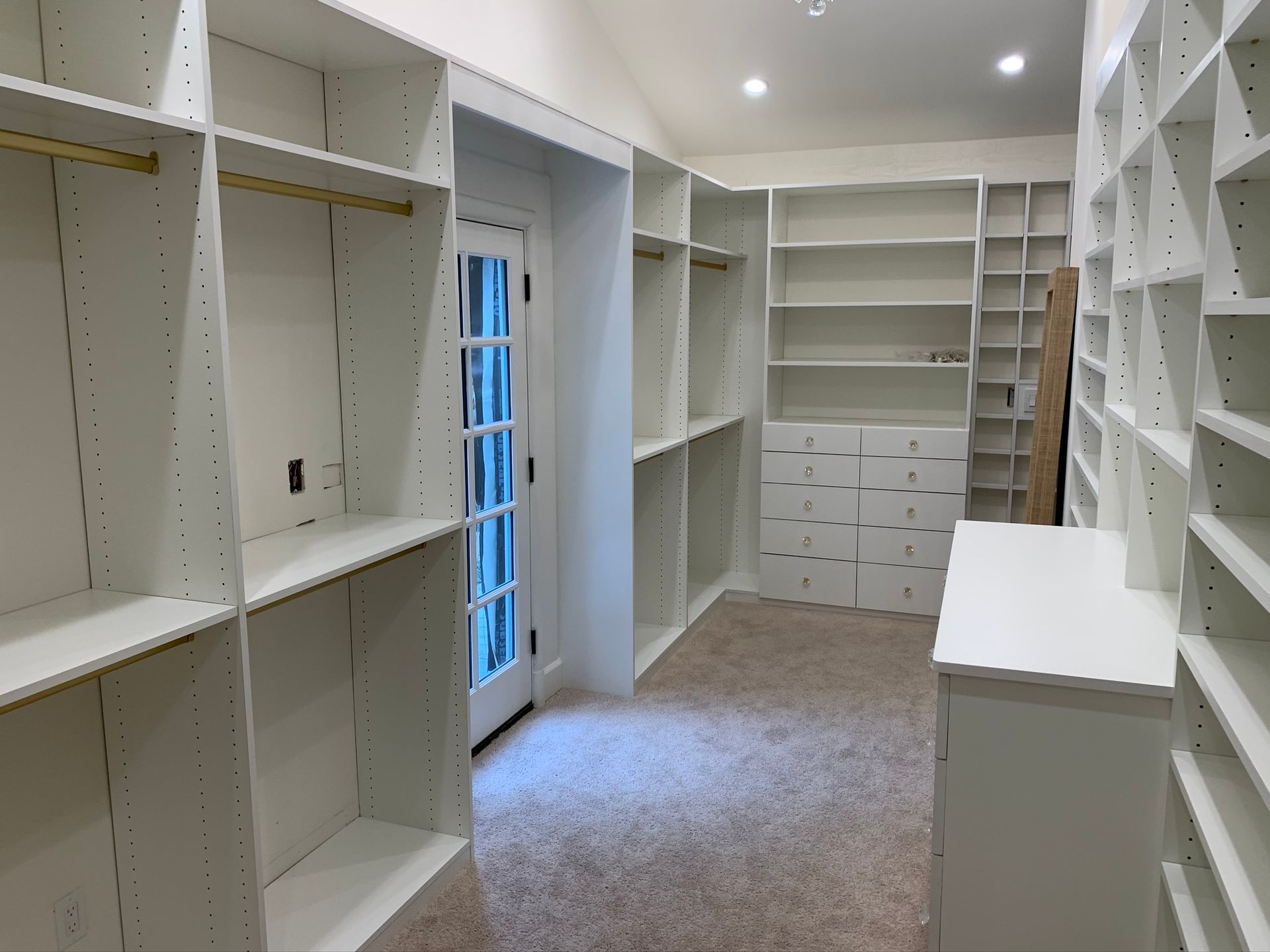 White walk-in closet with shelves and hanging rods; a door is visible in the back.