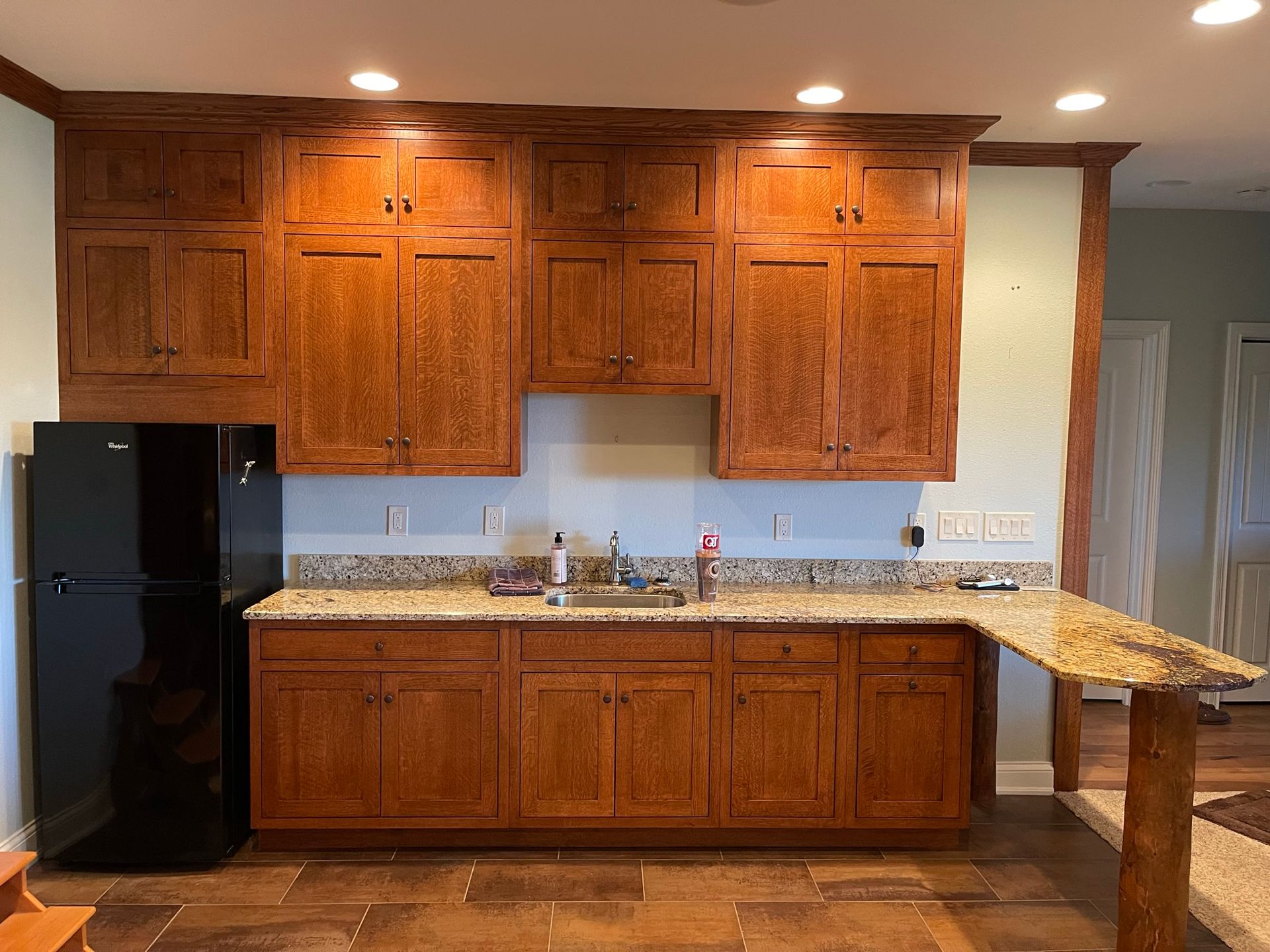 Kitchen with brown cabinets, black fridge, granite countertop, and breakfast bar.