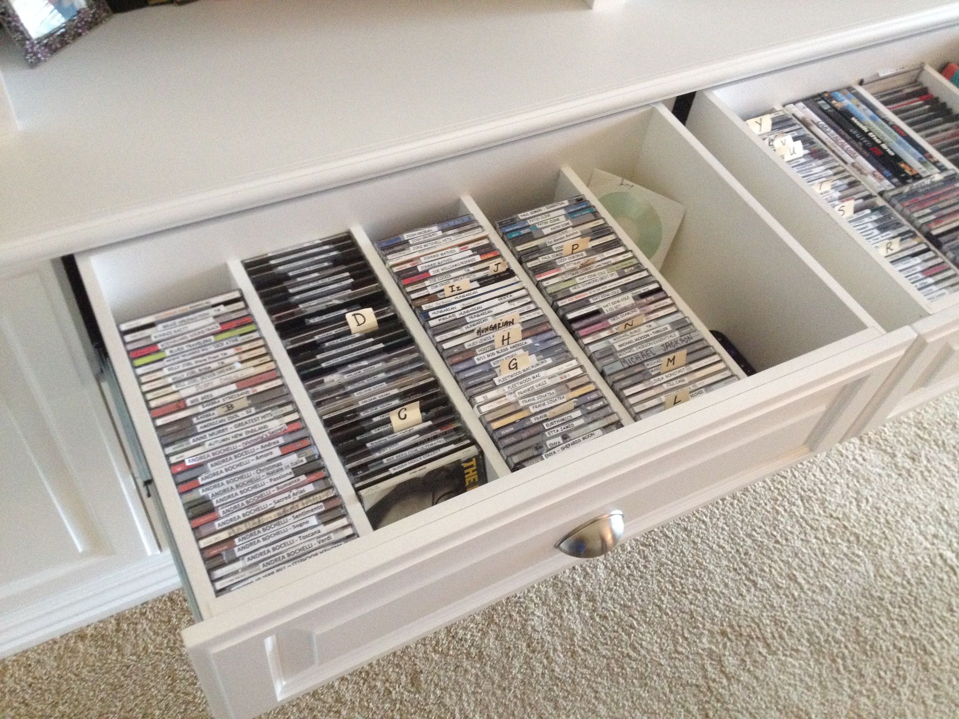 White cabinet drawer open, filled with vertically-stacked DVDs separated by dividers.