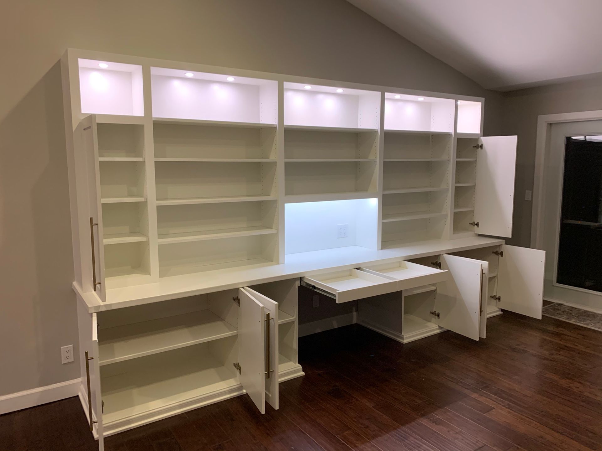 White built-in wall unit with shelves, cabinets, and a pull-out desk.