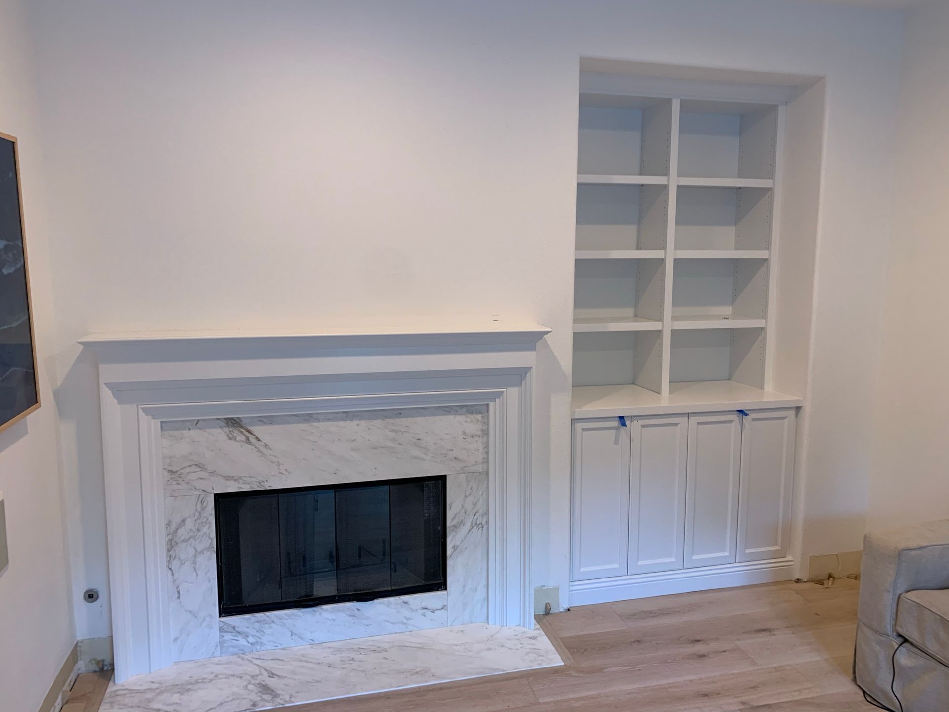 White fireplace with marble surround, built-in white bookshelves, and hardwood floor in a room.