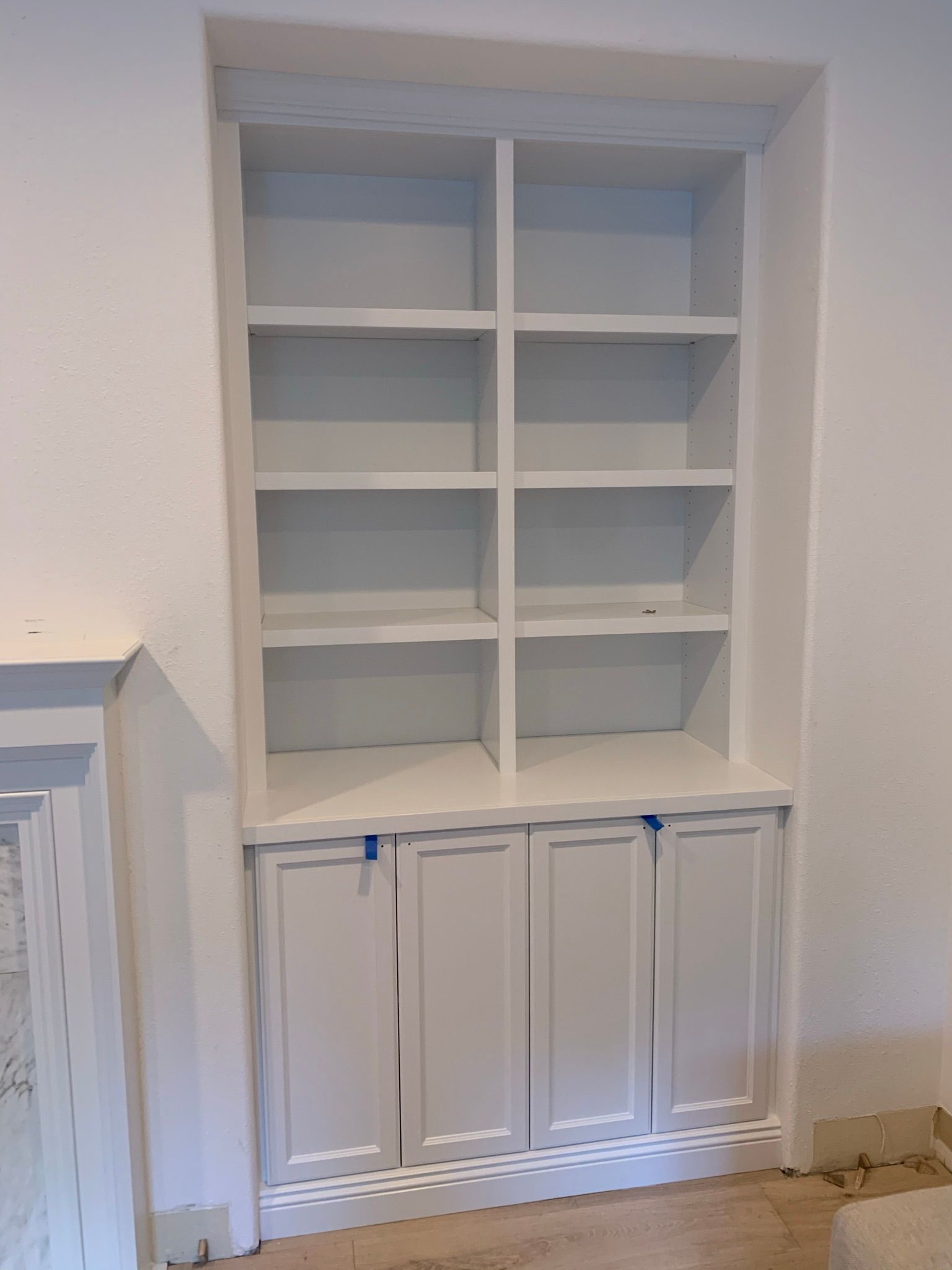 White built-in bookshelf with cabinet doors in a wall niche. Interior home setting.
