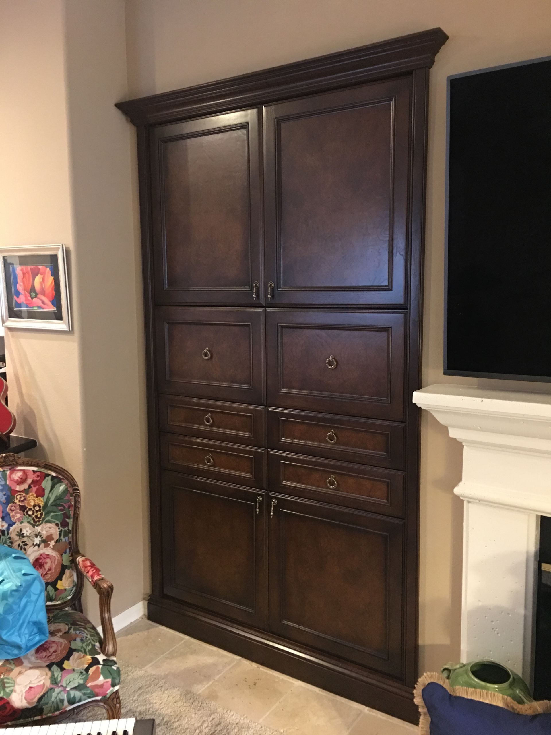 Dark wood corner cabinet with doors and drawers, next to a fireplace and a wall.