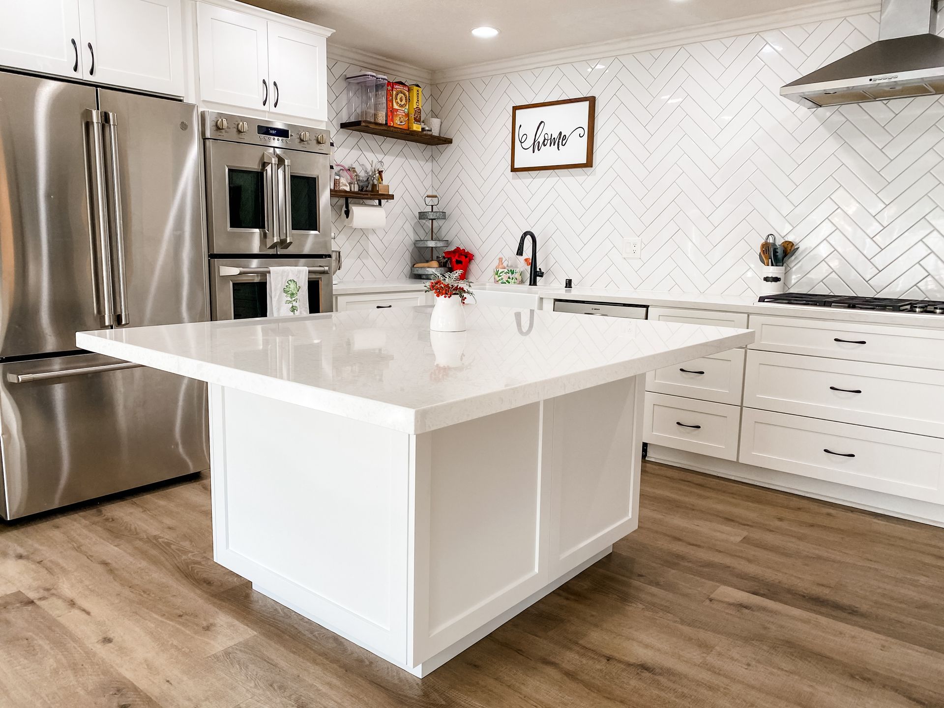 White kitchen with island; stainless steel appliances; herringbone backsplash; wood flooring.