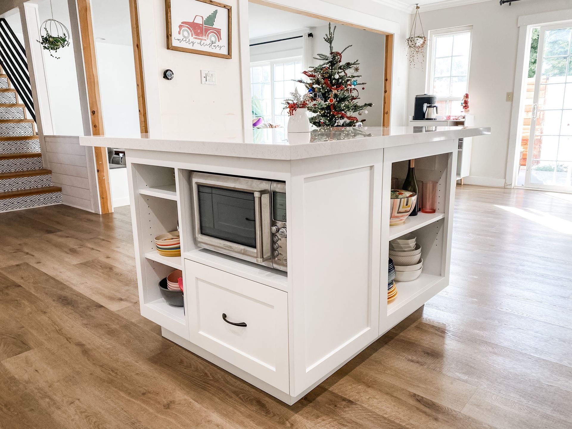White kitchen island with microwave and shelving, on wood floor.