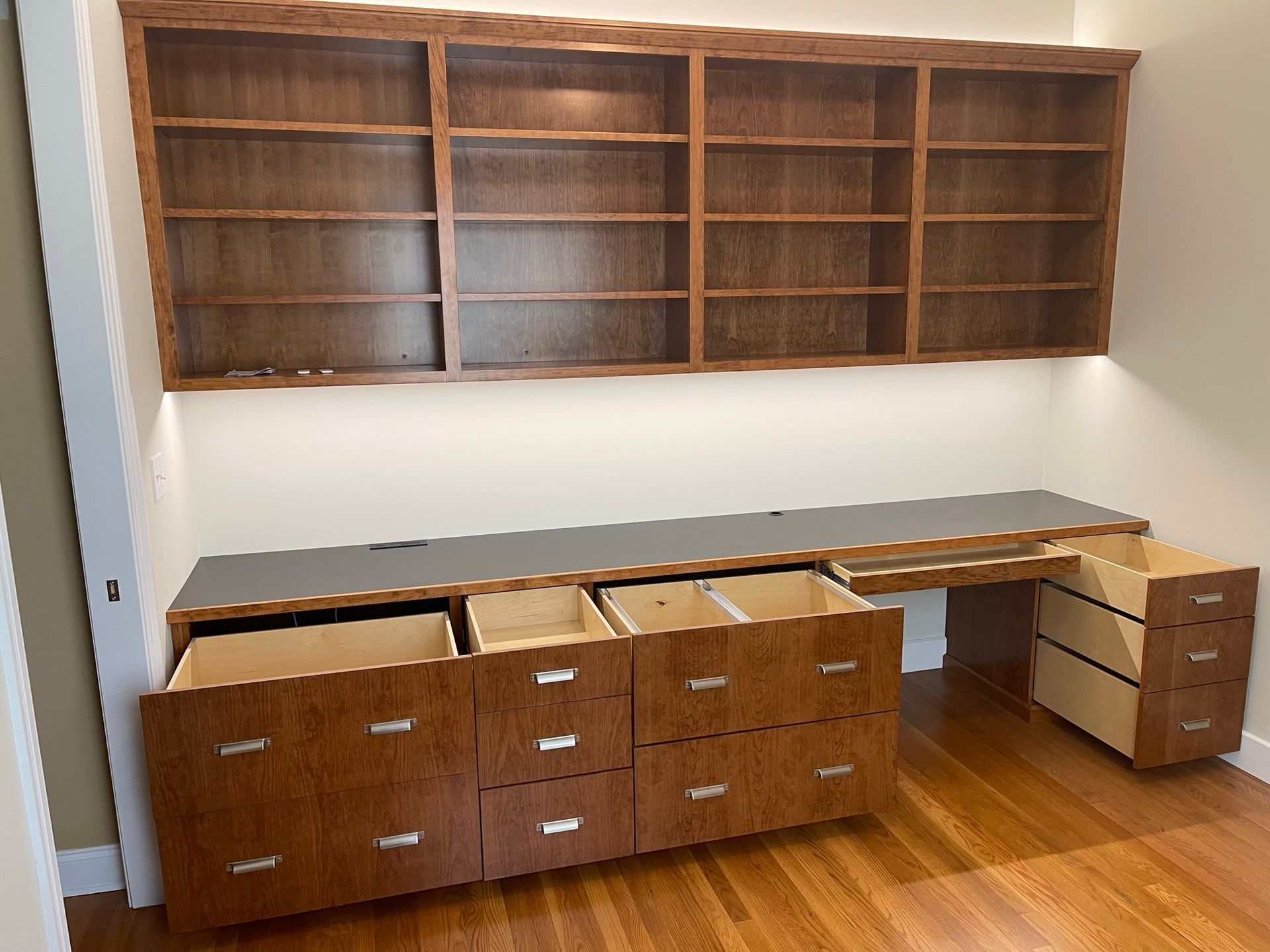 Built-in wooden desk and shelving unit with drawers and open shelves; brown wood and gray countertop.