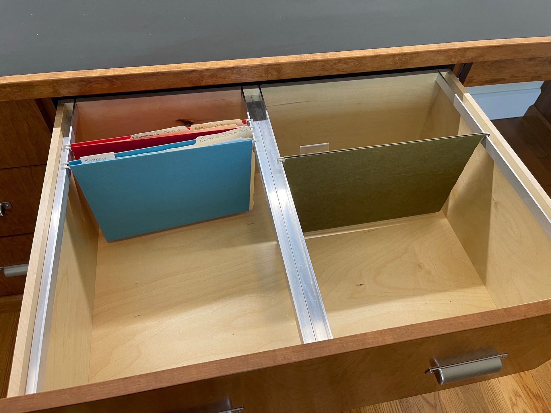Open desk drawer with file folders and metal dividers.