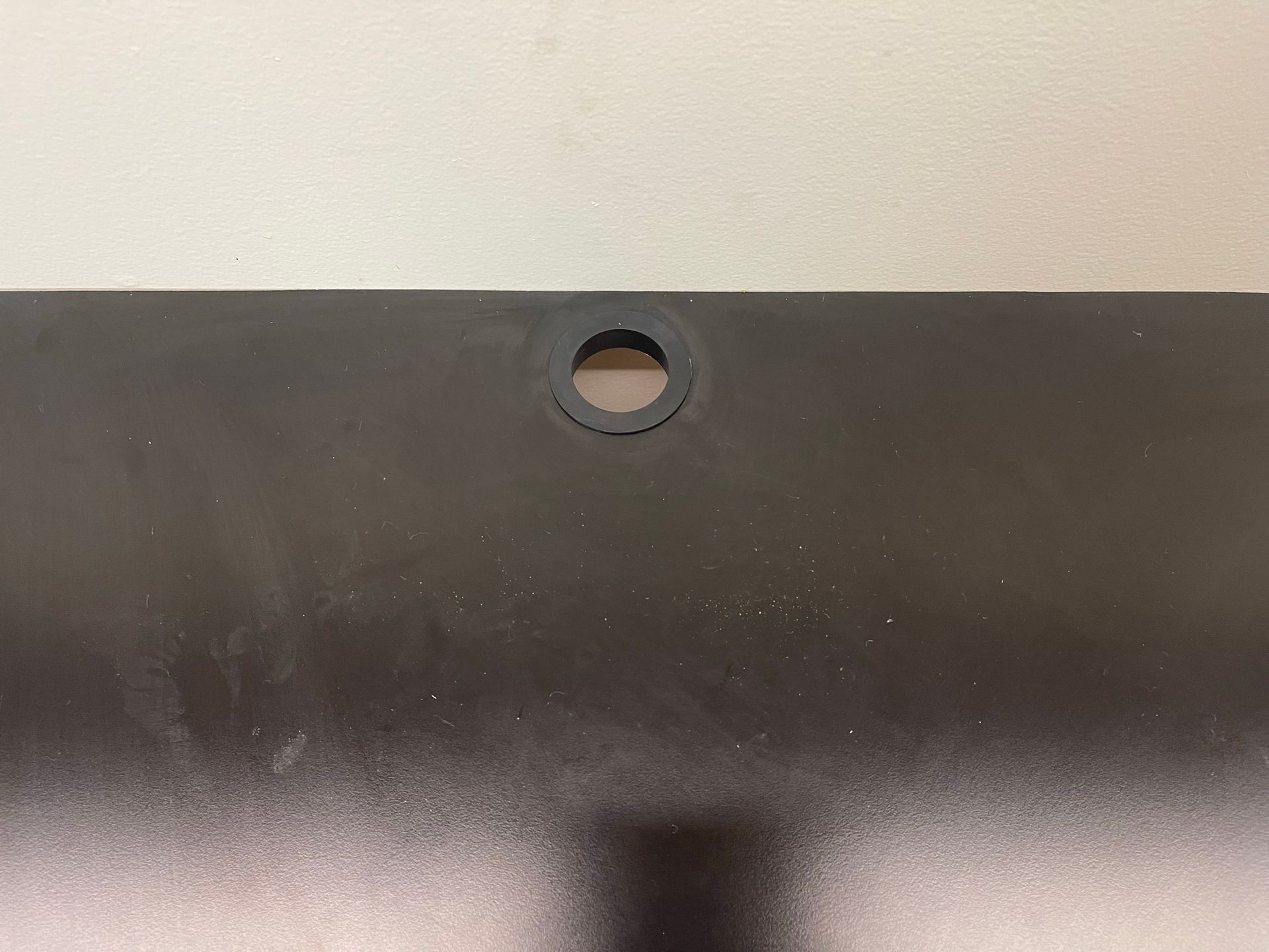 Black panel with a circular rubber grommet in the center. Light-colored wall in the background.