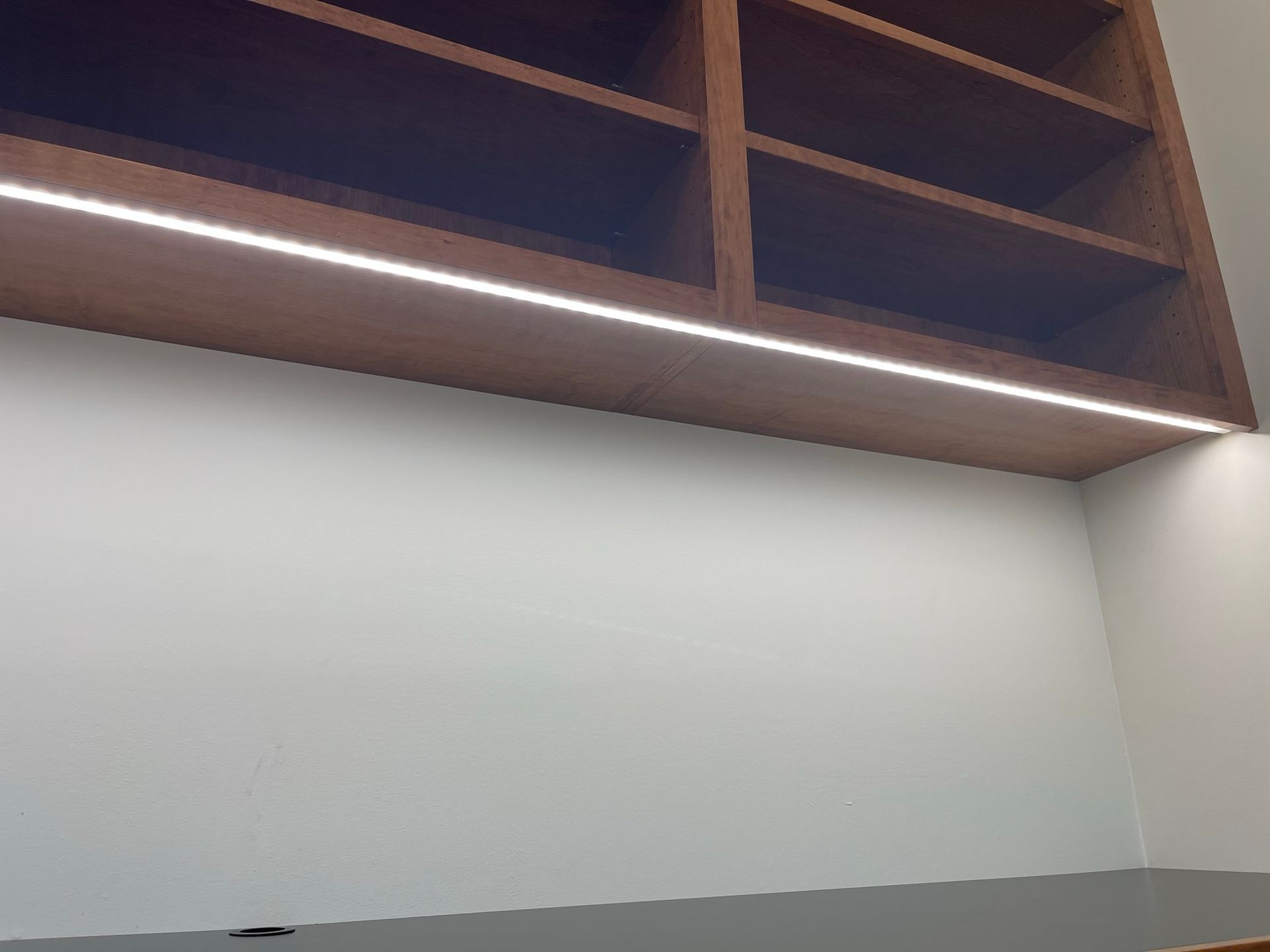 Built-in wooden shelves with bright LED strip lighting over a white wall and countertop.