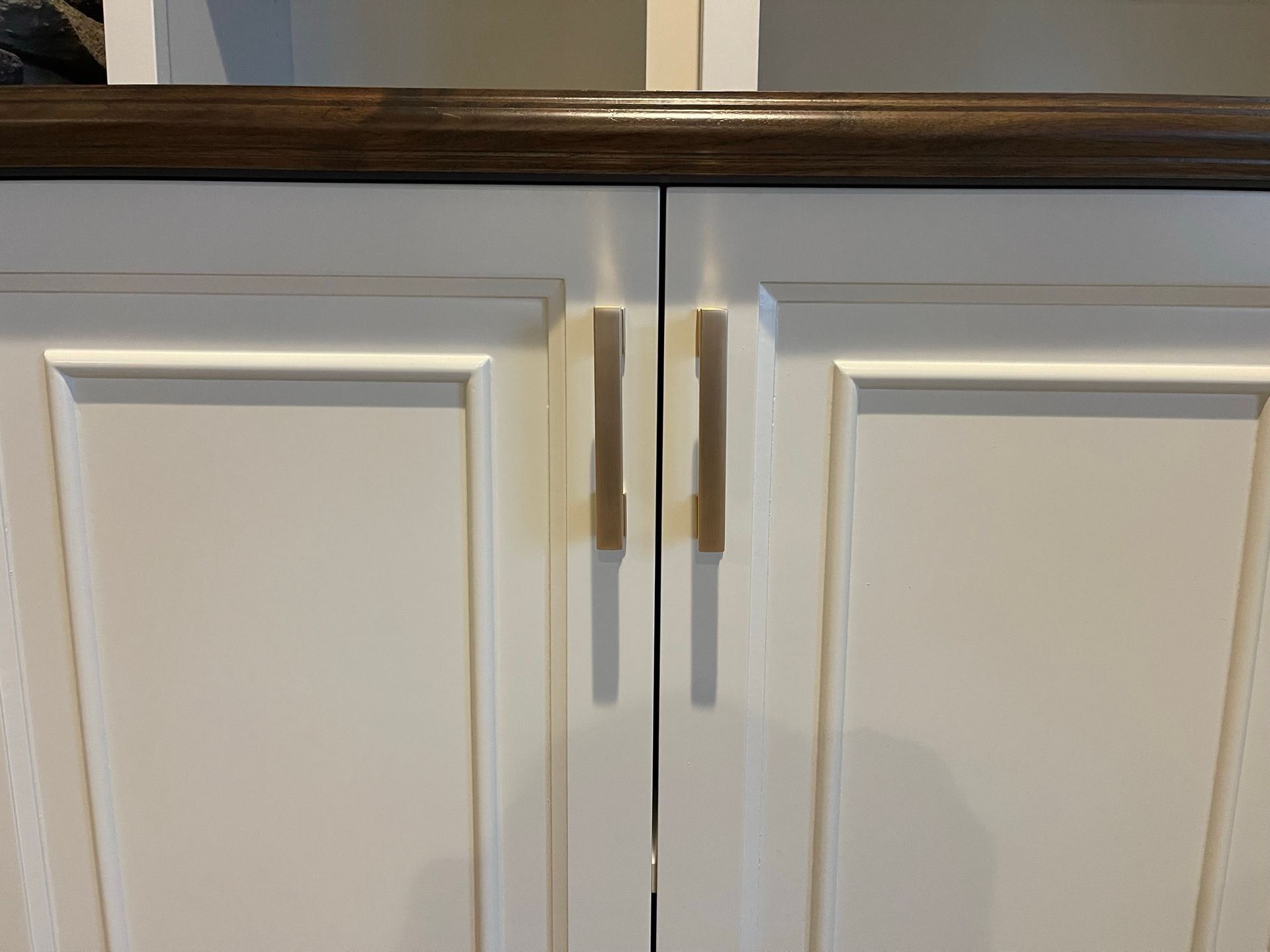 White cabinet doors with gold-toned handles and a dark brown countertop.