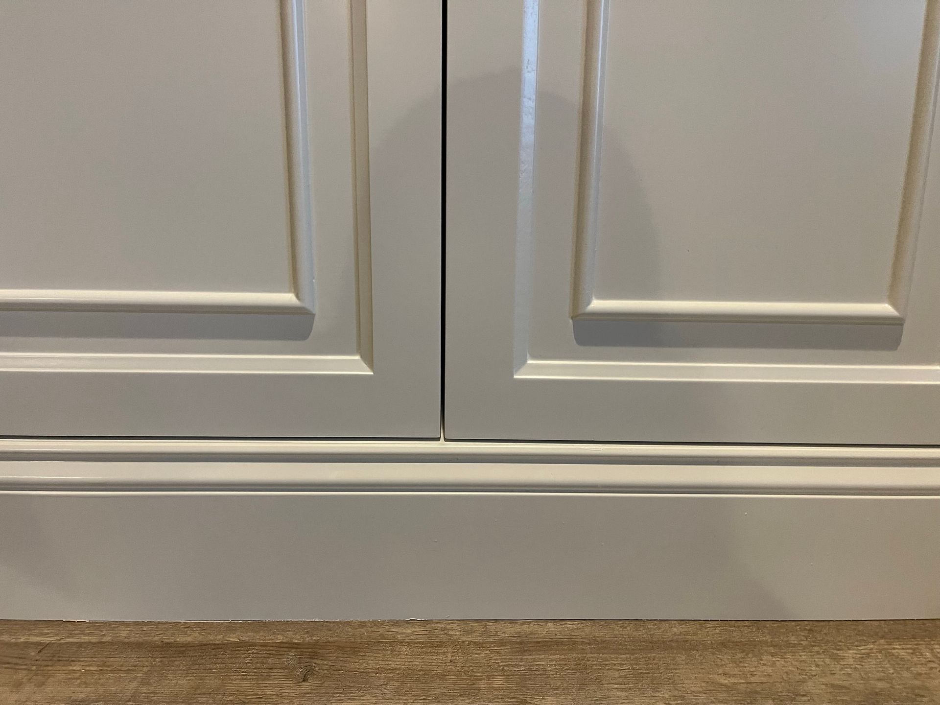 Close-up of white kitchen cabinet doors with a decorative base, set against a light brown floor.