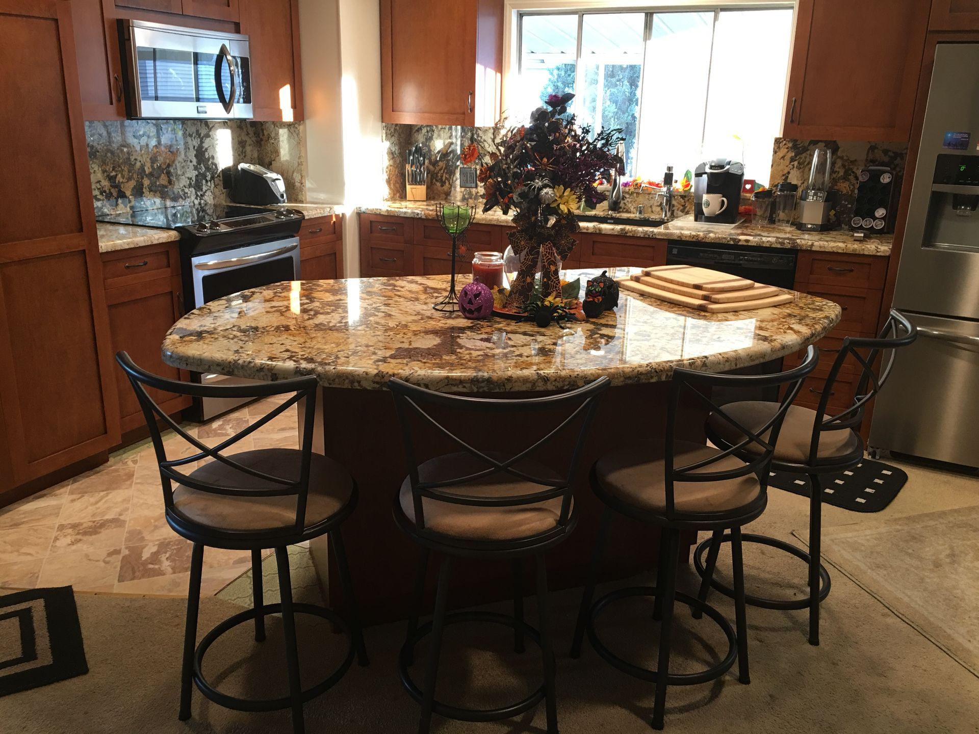 Kitchen with brown cabinets, granite island, and four bar stools.