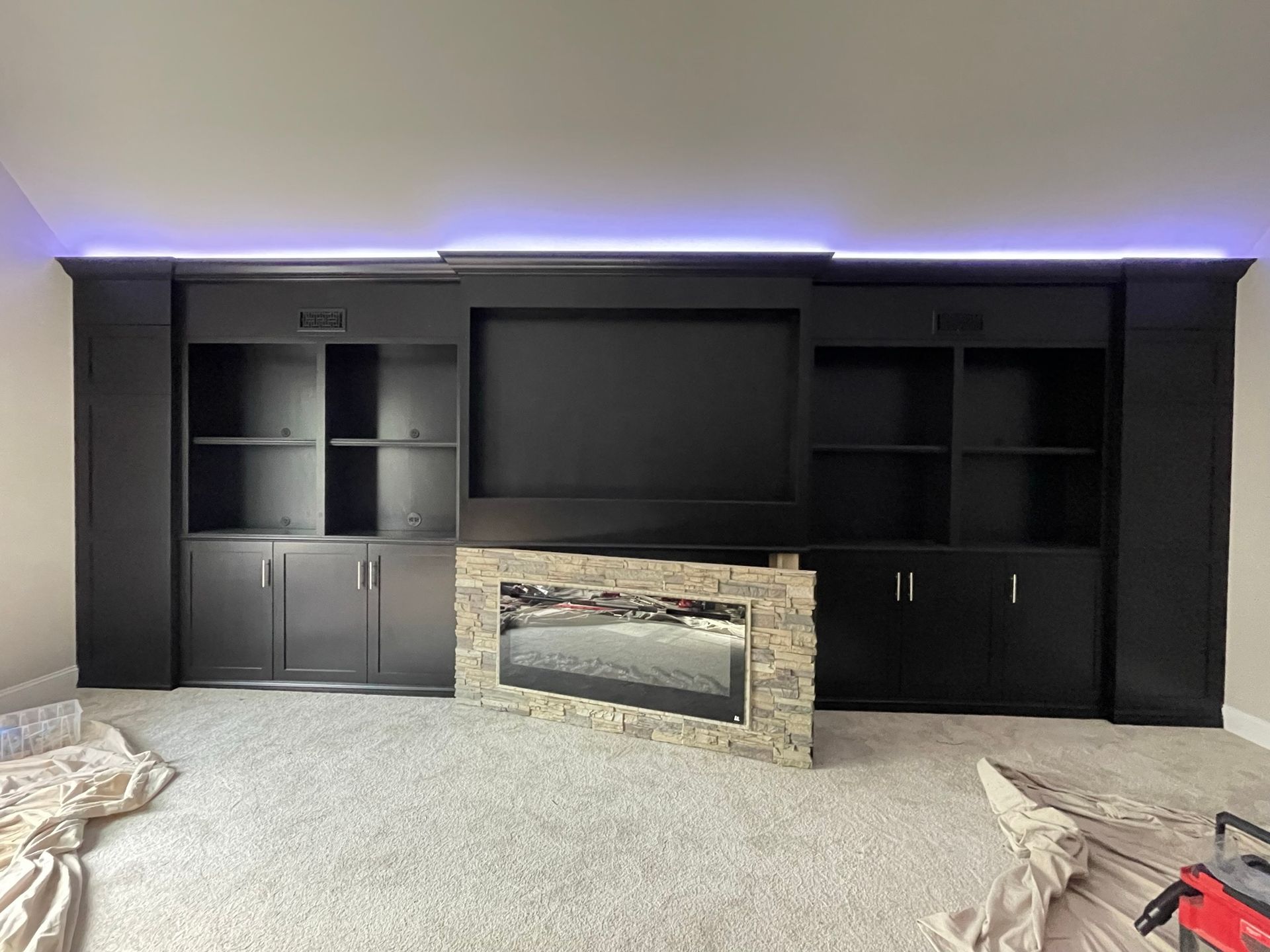 Black entertainment center with shelves, cabinets, and a fireplace, against a light gray wall and carpet.