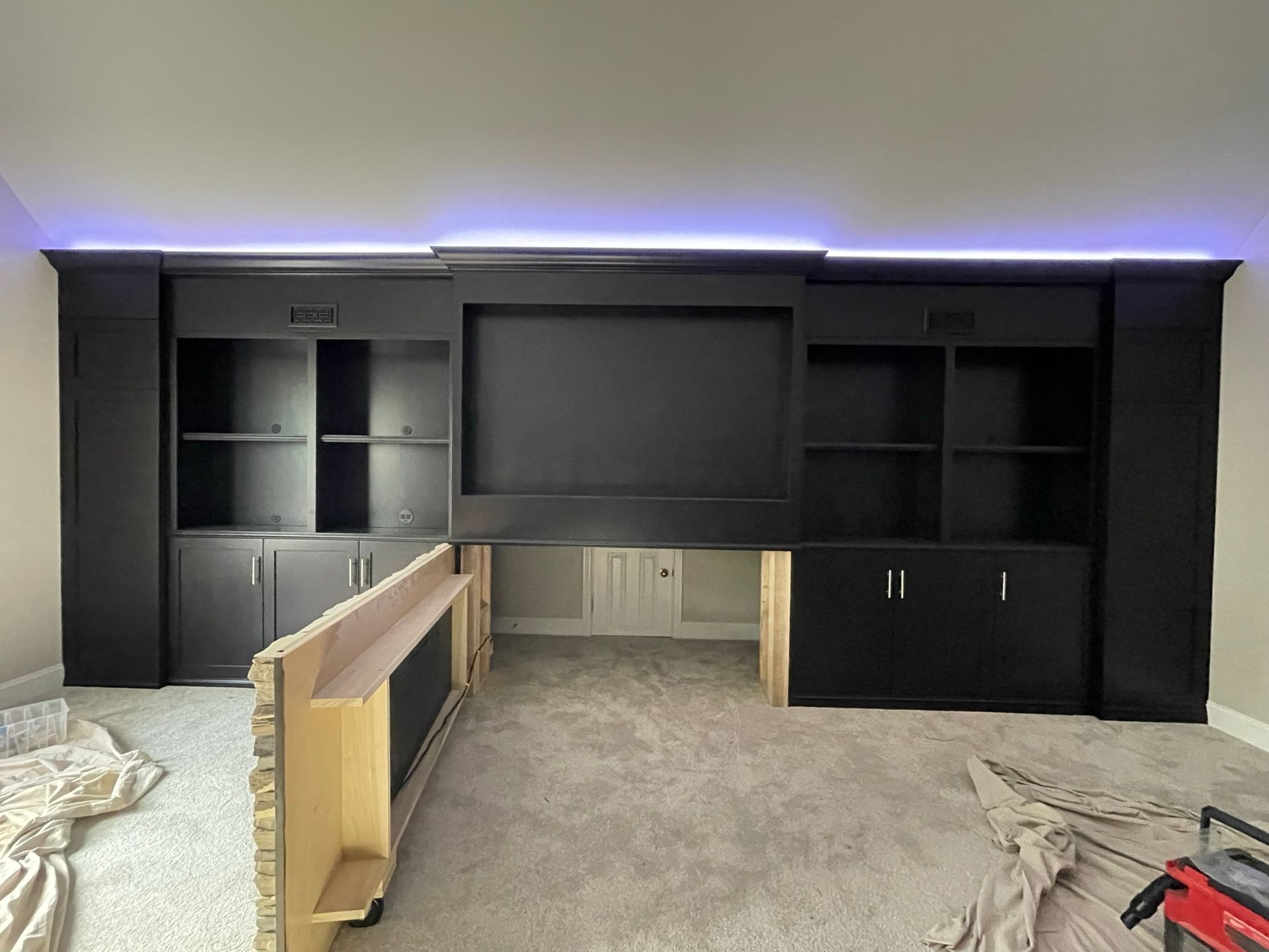 Black entertainment center with shelving and recessed TV area, under construction, against a light wall.