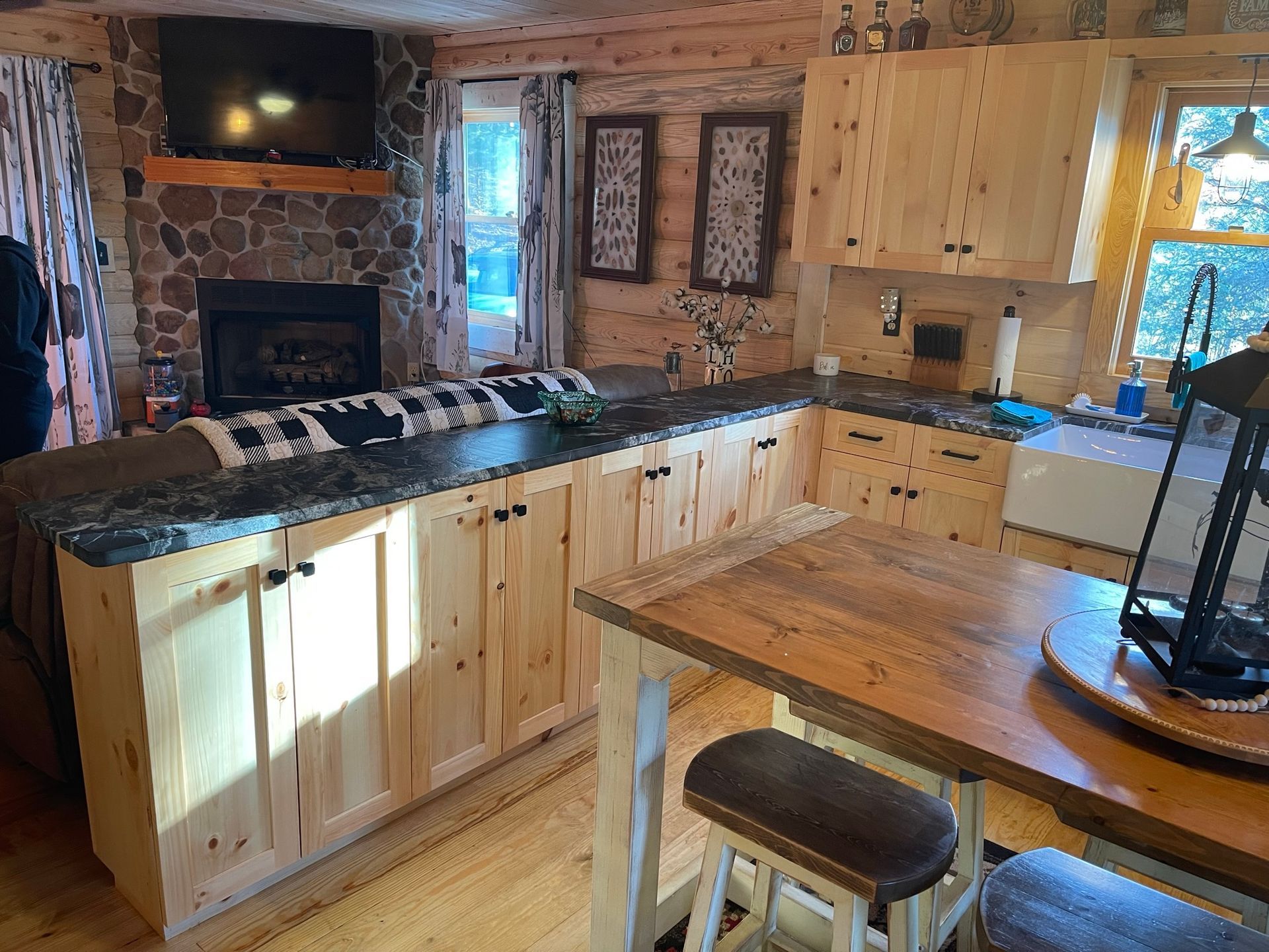Kitchen in a log cabin with wooden cabinets, a dark countertop, and a small dining table.