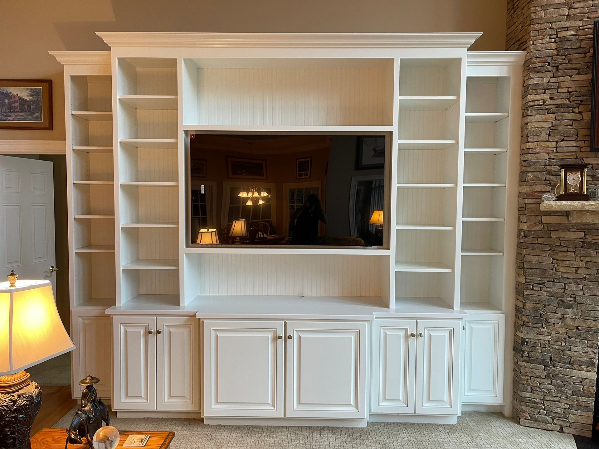 White built-in entertainment center with shelves, cabinets, and a TV; set against a textured stone wall.