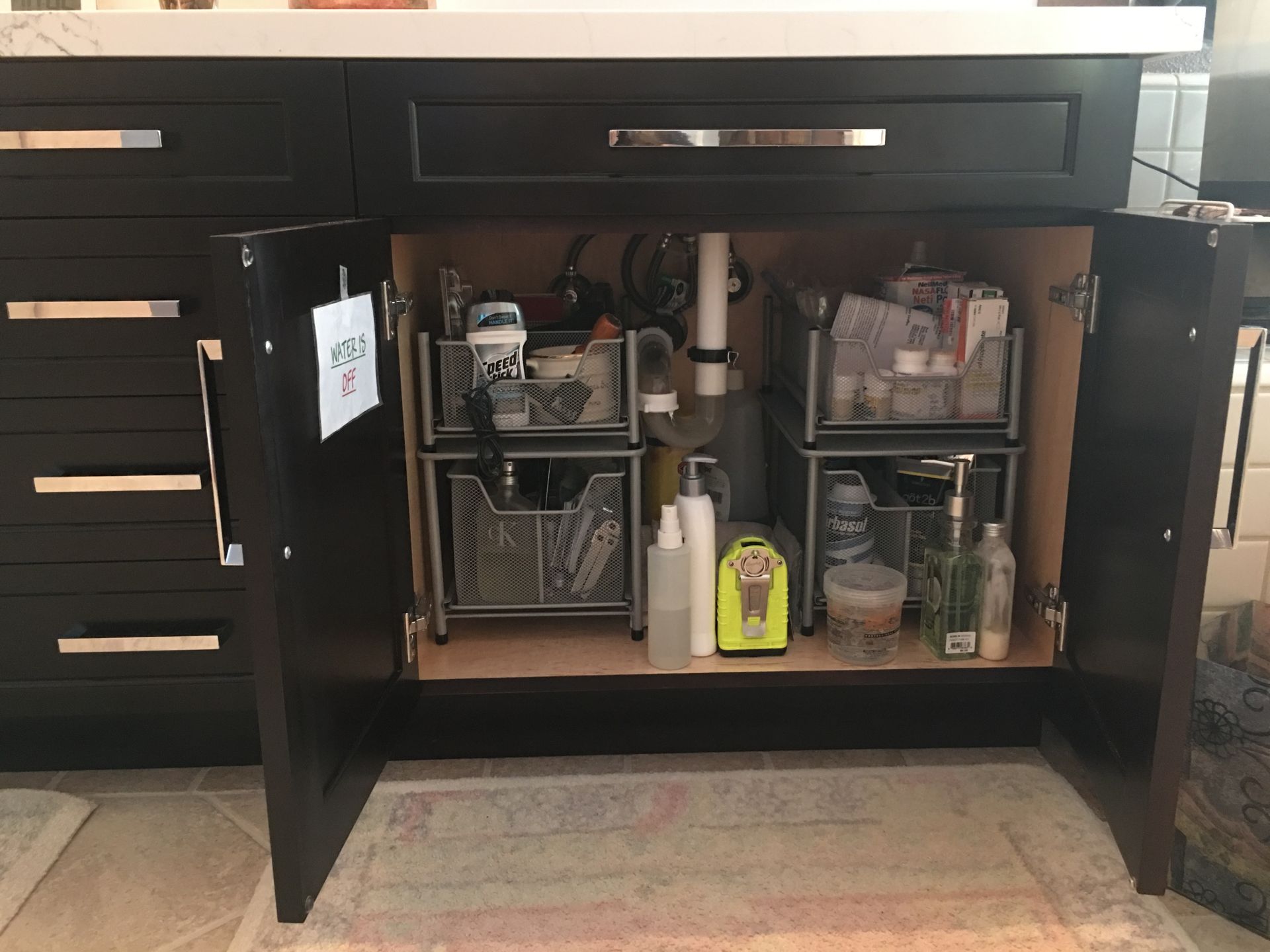 Bathroom vanity cabinet with open doors, showing organized storage bins under the sink.
