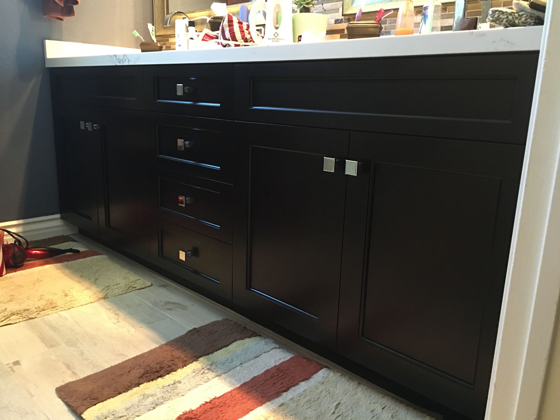 Dark brown bathroom vanity with white countertop, chrome hardware, drawers, and cabinet doors.