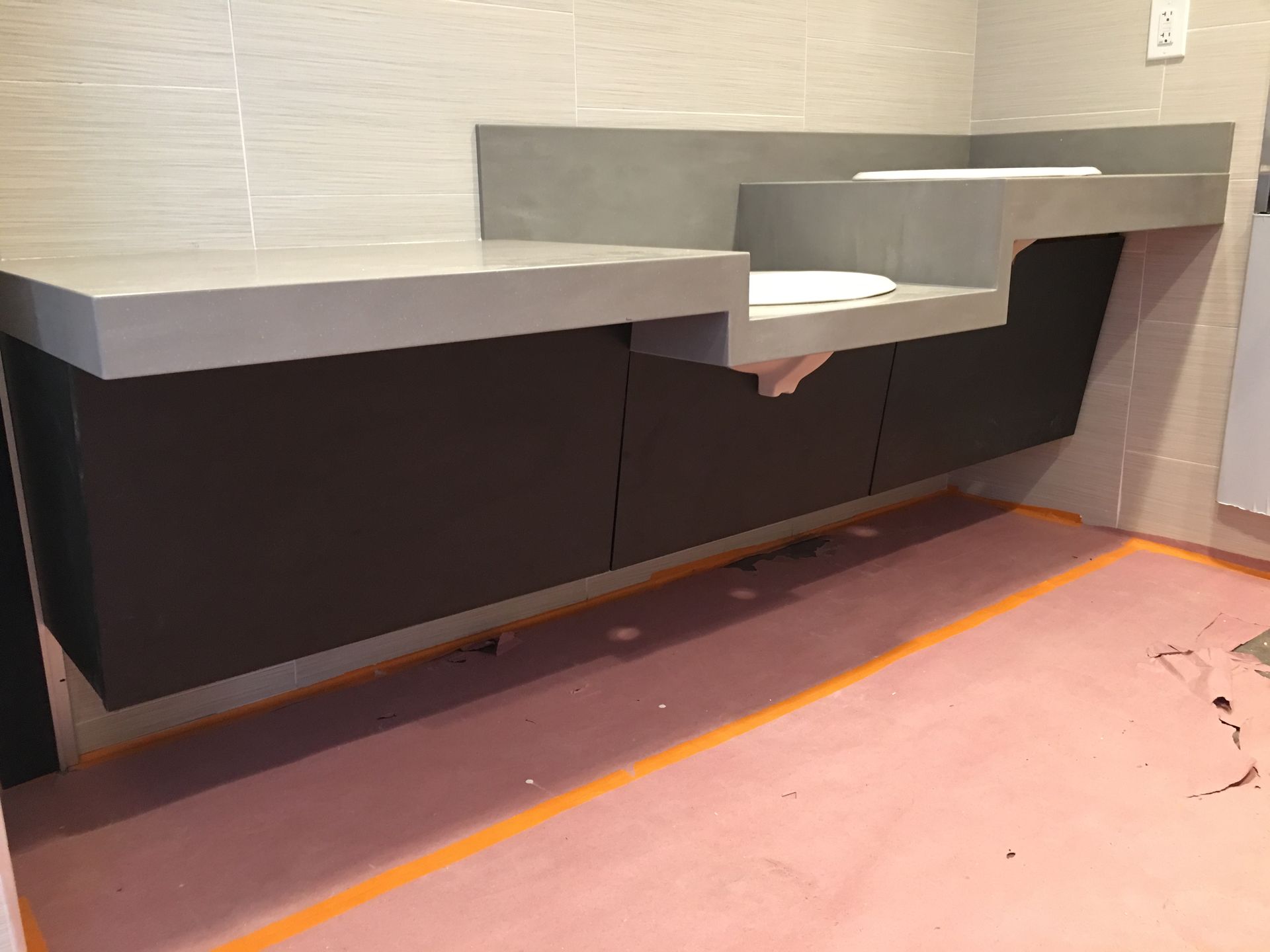 Bathroom vanity with dark cabinets and gray countertop. Pink flooring with orange outline.