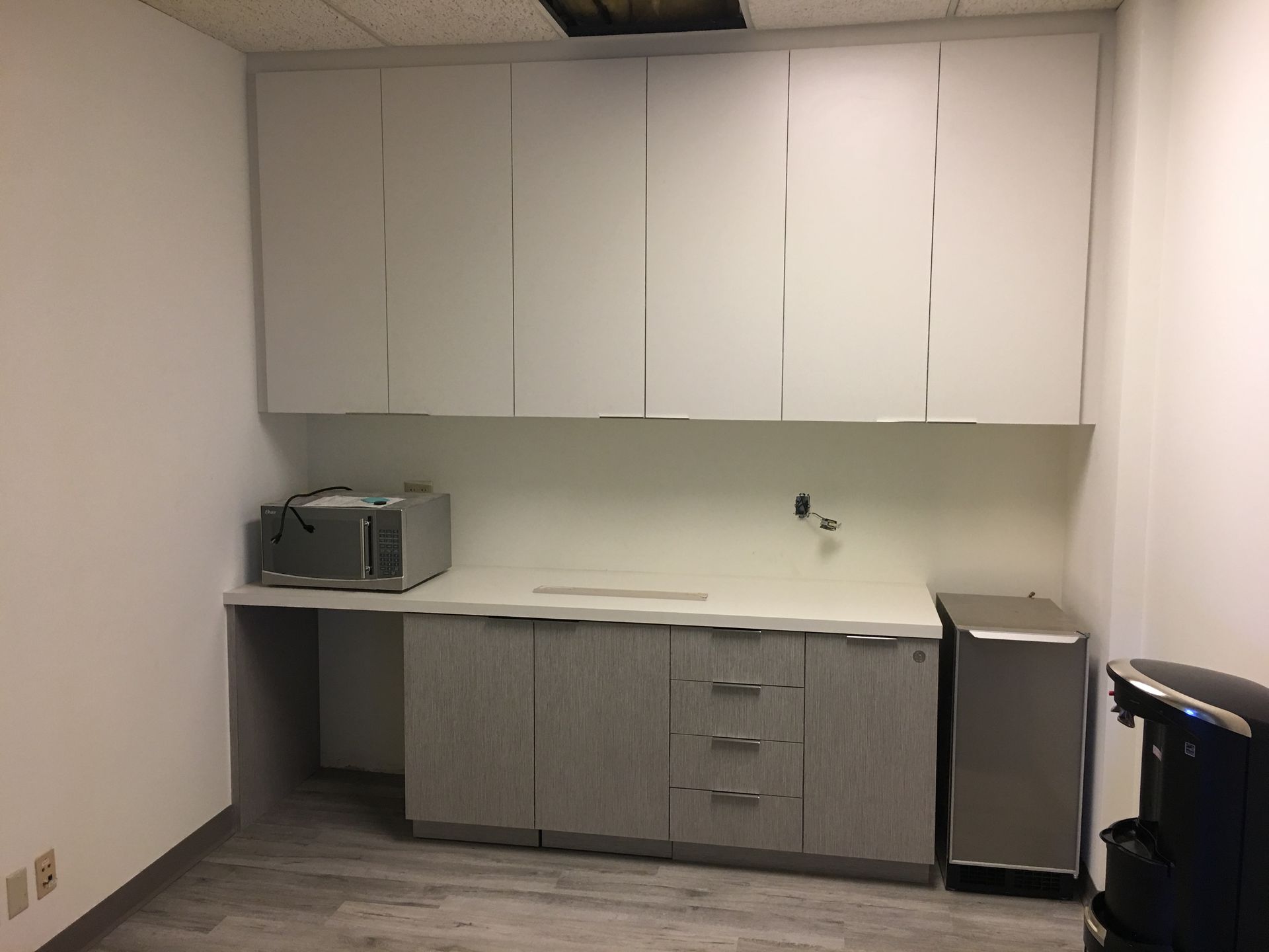 A small office kitchenette with white cabinets, a microwave, countertop, and coffee maker.