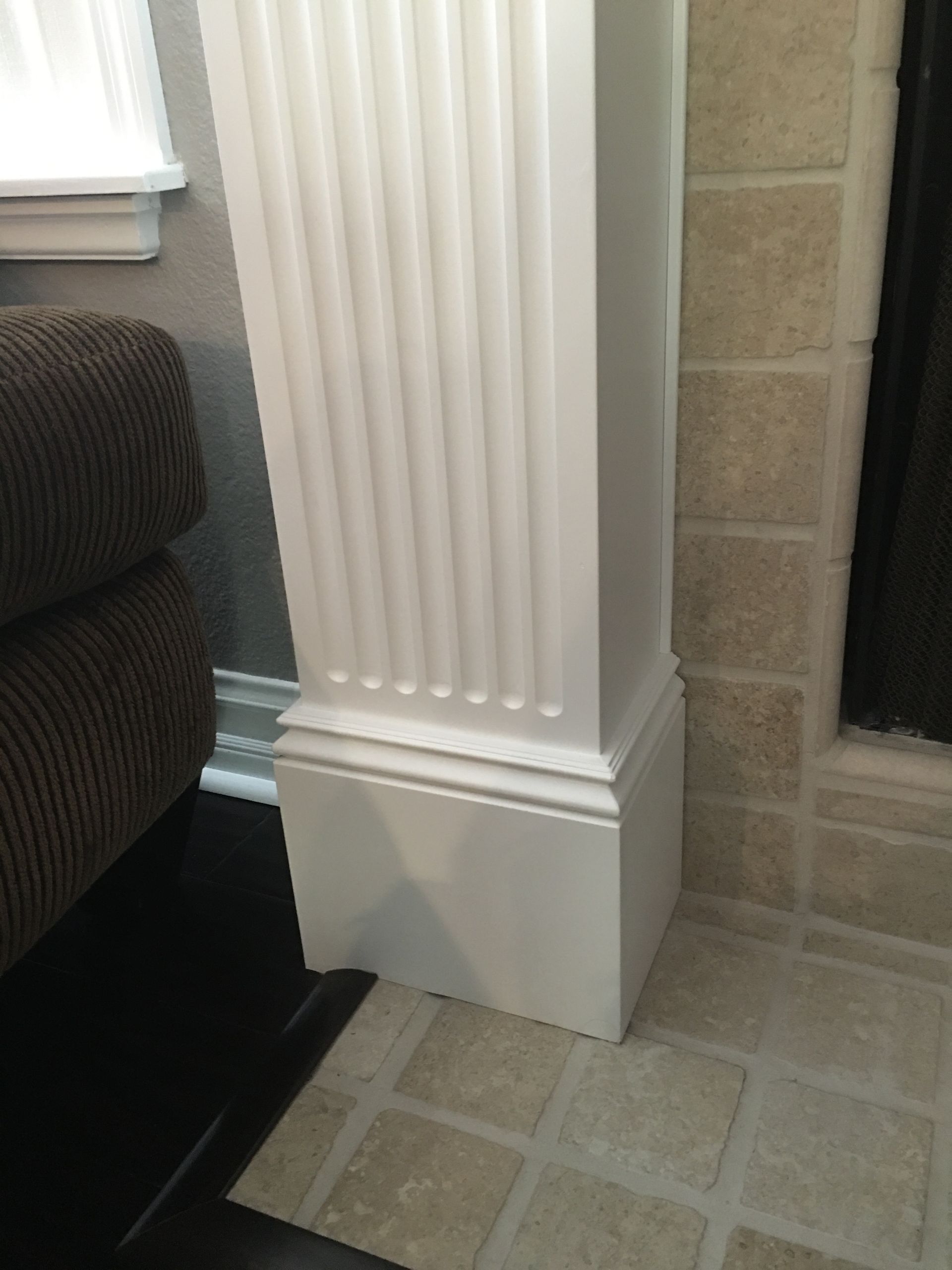 White pillar next to a brown upholstered arm of a couch. Light-colored tile flooring.