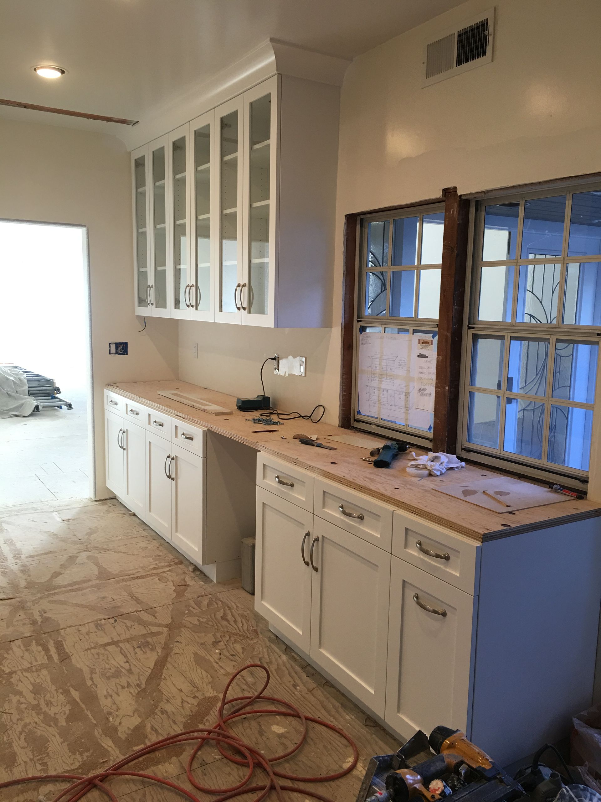 White kitchen cabinets with wooden countertops and windows, under construction.
